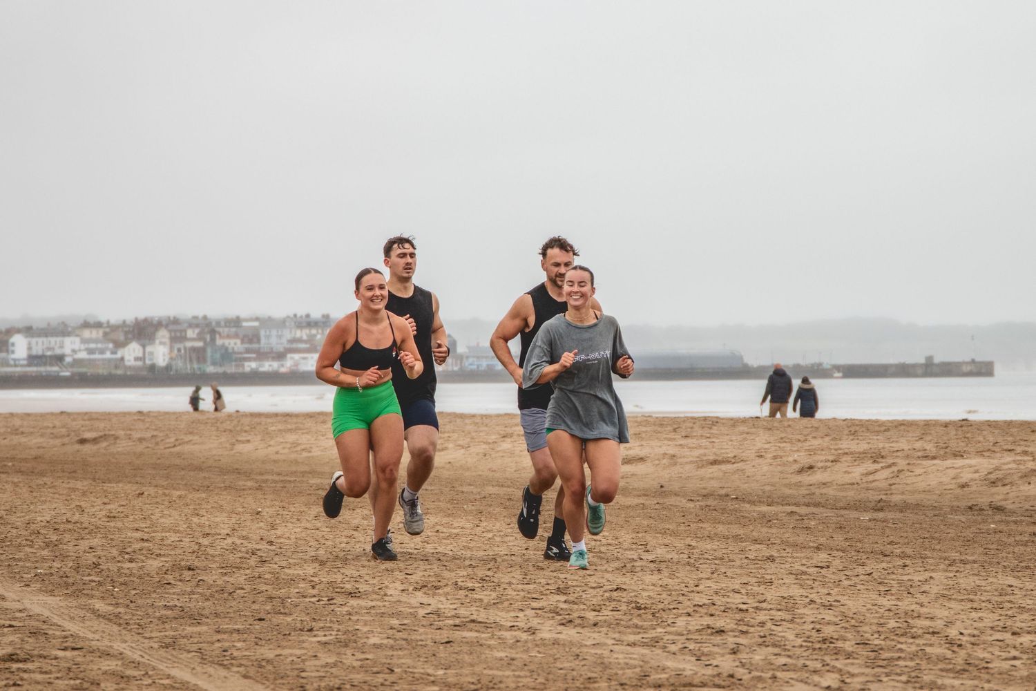 Athletes train using bear crawl exercises on sandy beach during outdoor workout session.