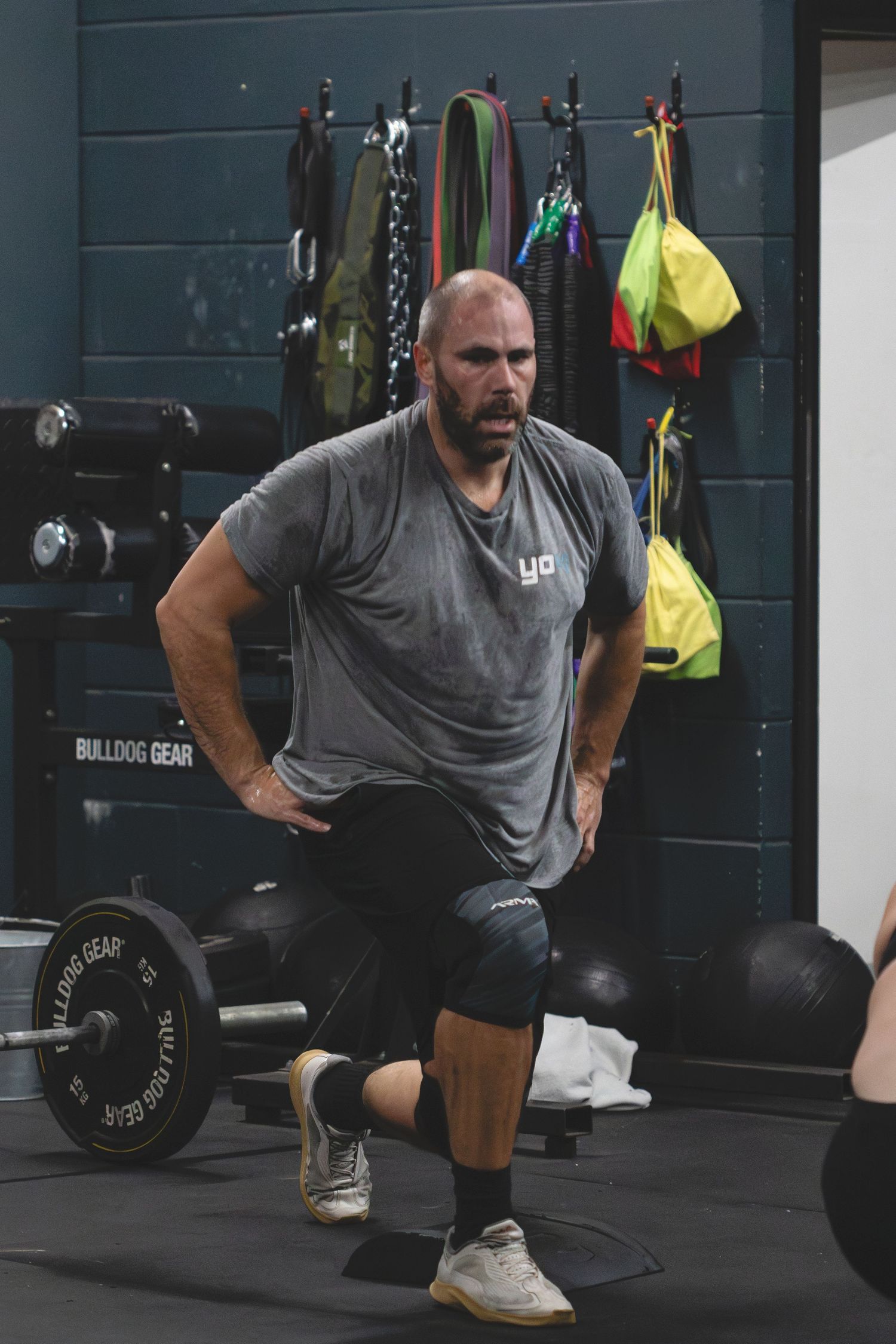 Someone stretches and prepares for a workout at a CrossFit gym with barbells and equipment in the background.