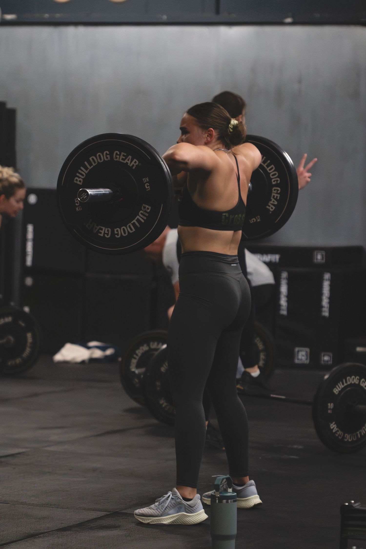 Athletic woman performs a barbell squat exercise wearing black workout attire in a dark gym setting.