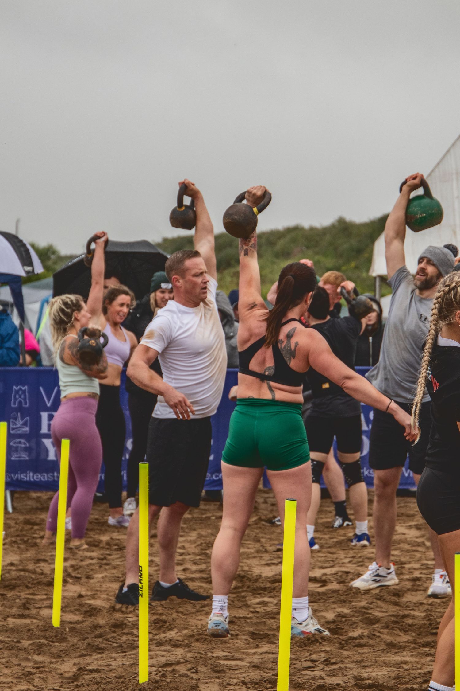 Group of fitness enthusiasts on beach perform synchronized beer drinking exercises during outdoor workout event.