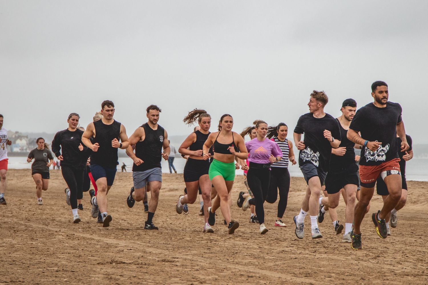 A group of runners participate in an outdoor race on a dirt trail under an overcast sky.