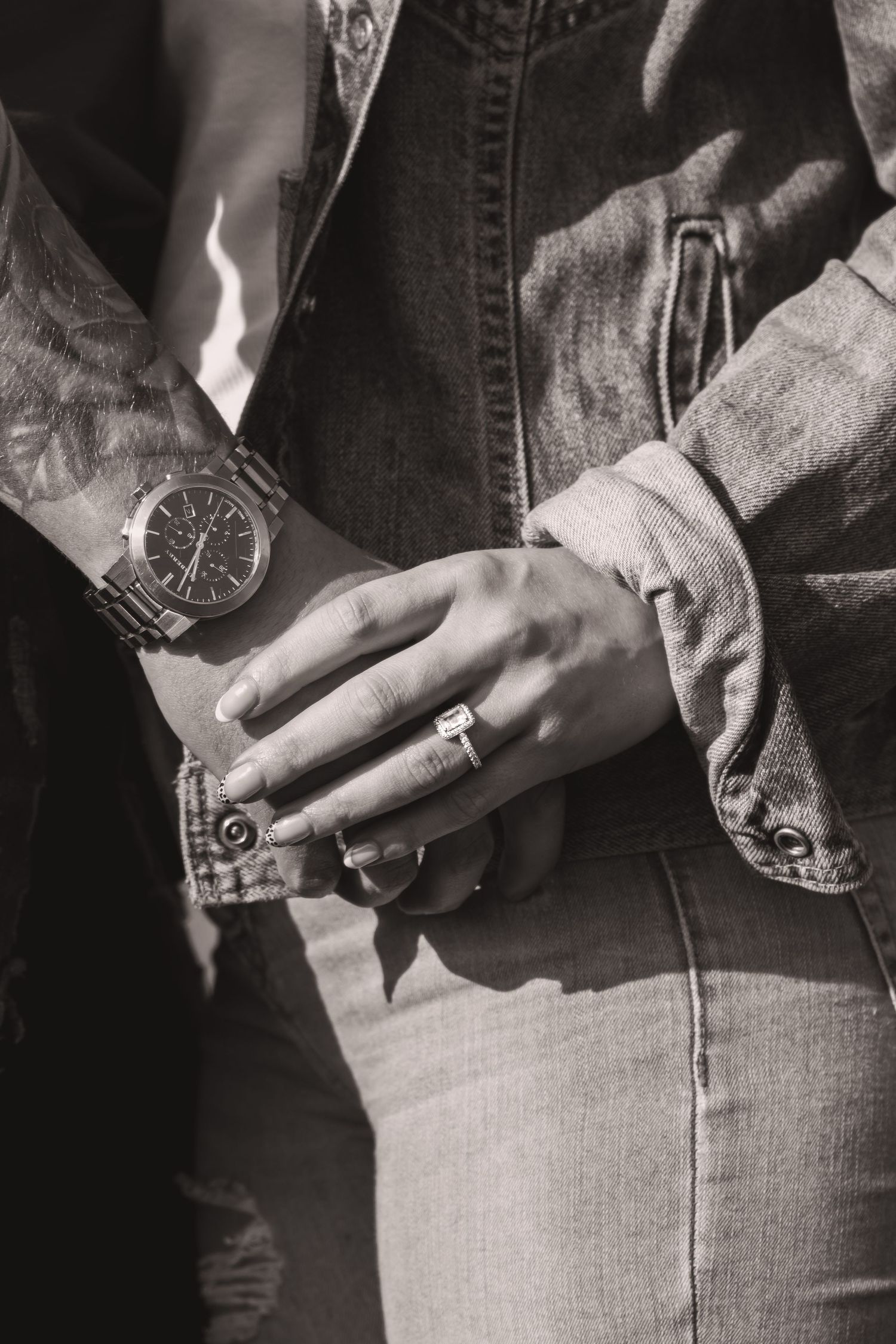 Close-up of clasped hands showing a watch and engagement ring against denim clothing.