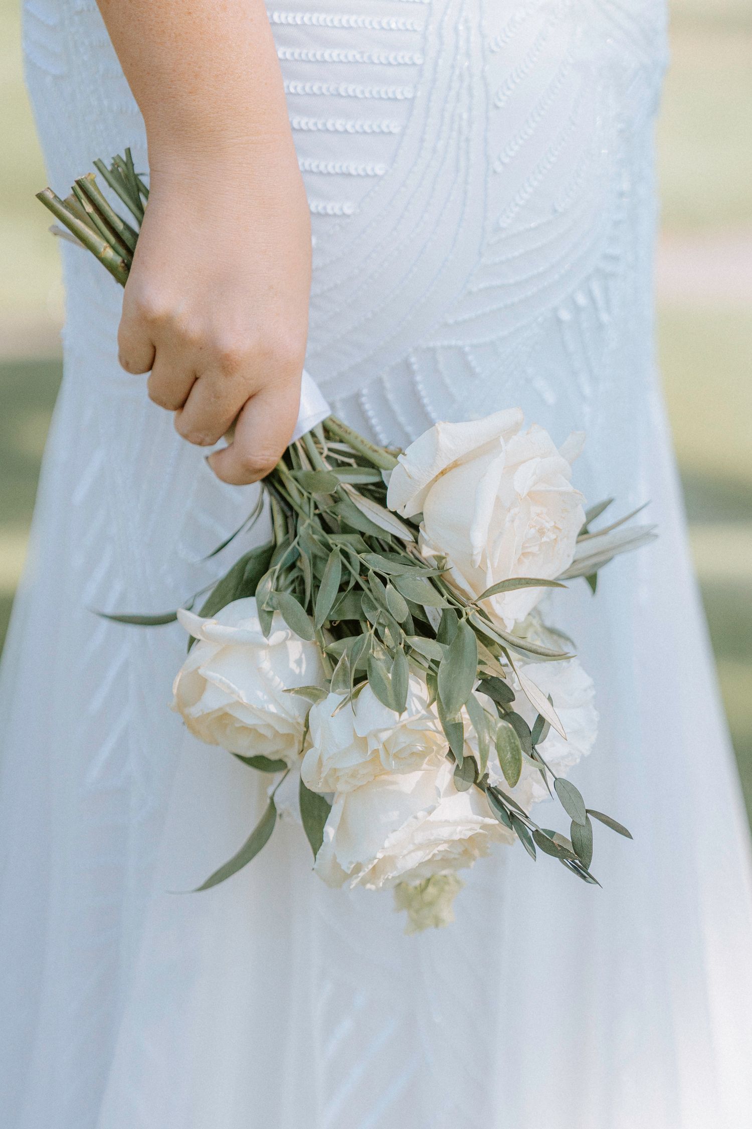 Close-up shots of a white wedding bouquet with roses and greenery against a white dress.