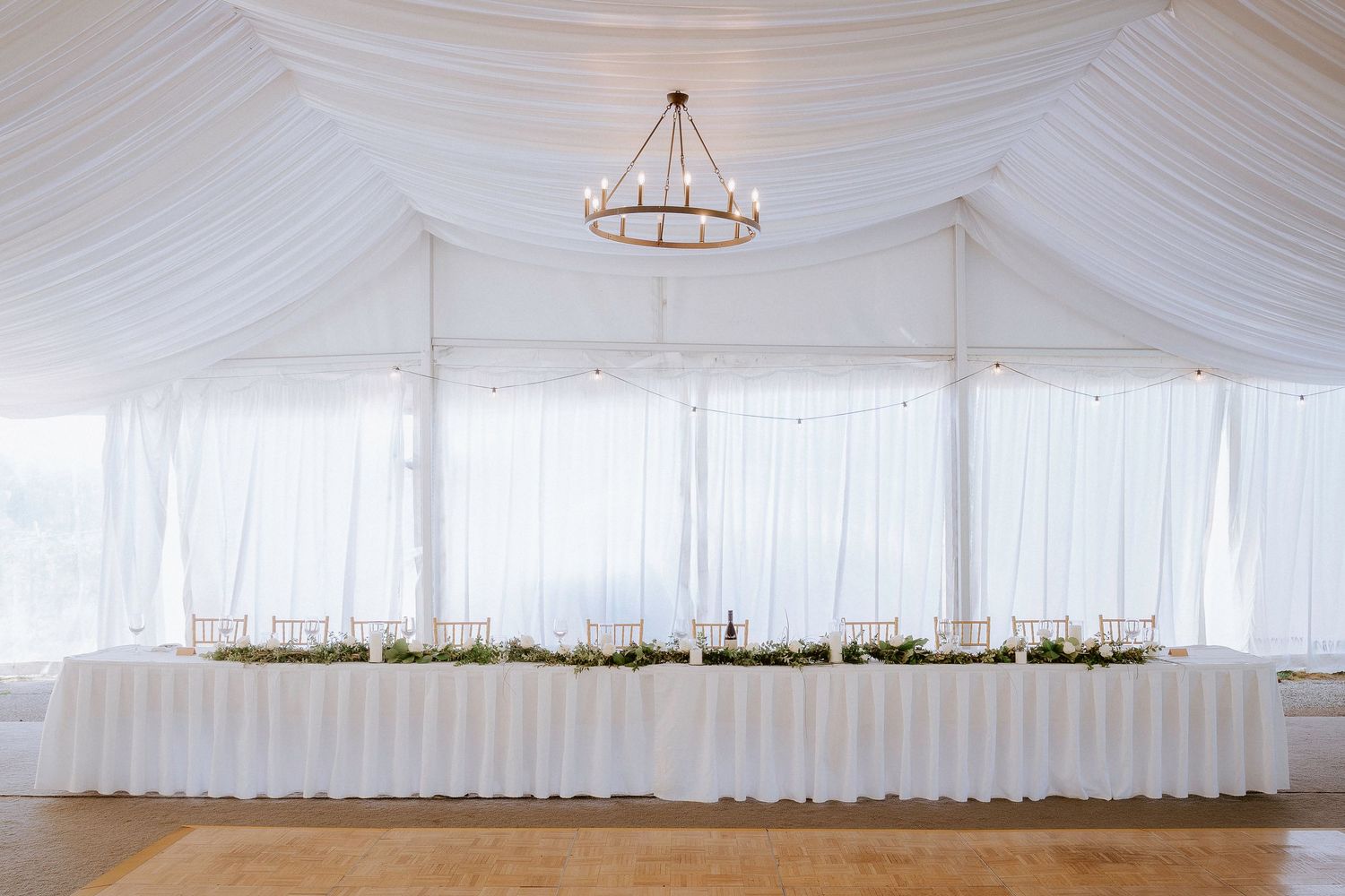 Elegant white wedding tent interior with draped fabric ceiling and crystal chandeliers creating a romantic atmosphere.