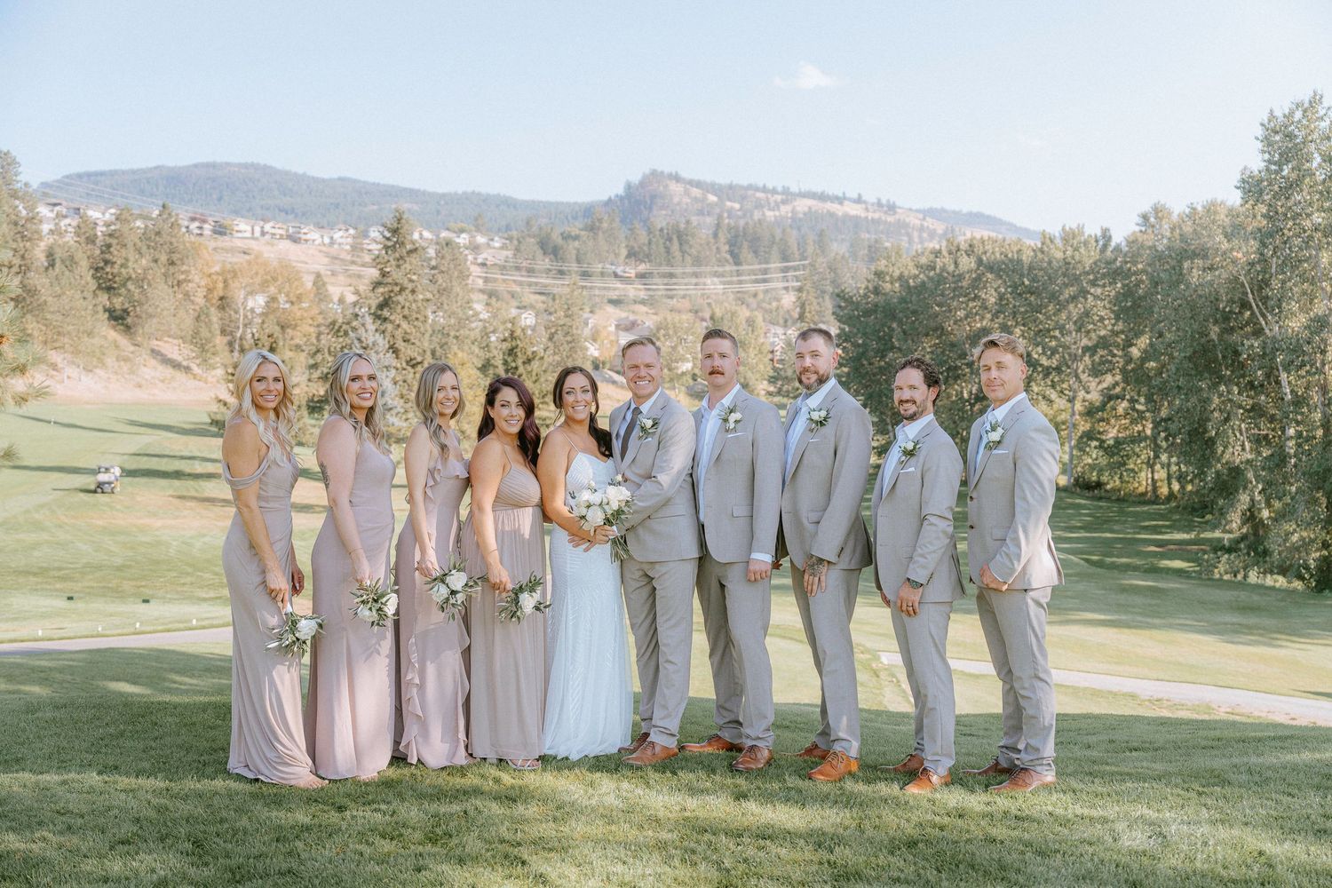 Wedding party in gray and white attire posed together on a scenic golf course with mountain backdrop.