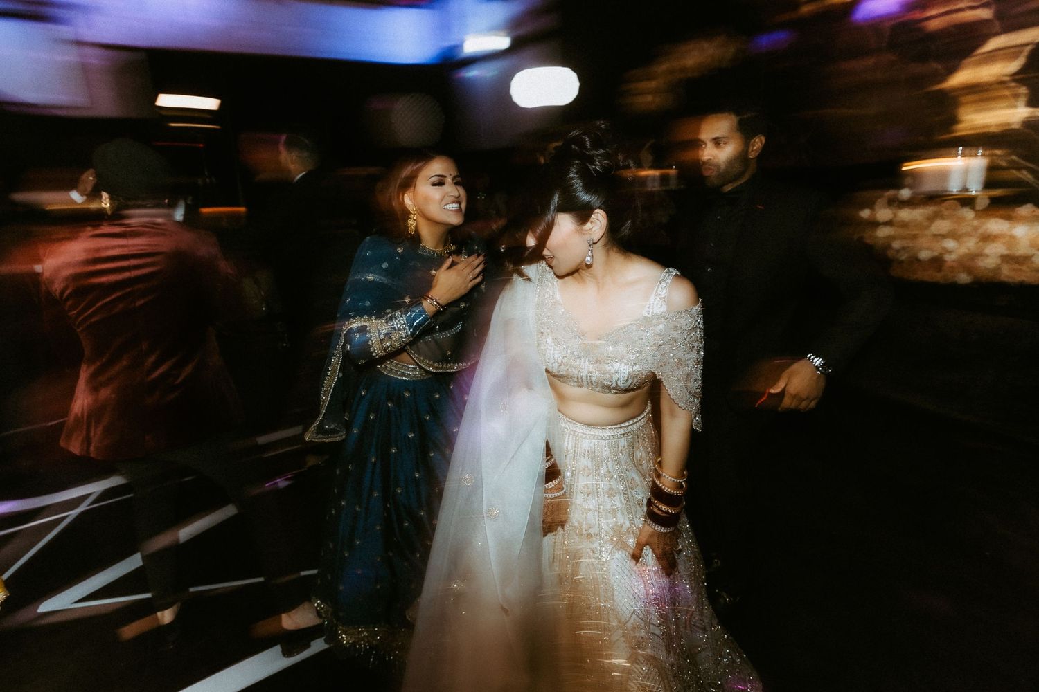 Wedding celebration with dancing guests under moody lighting at an indoor reception venue.