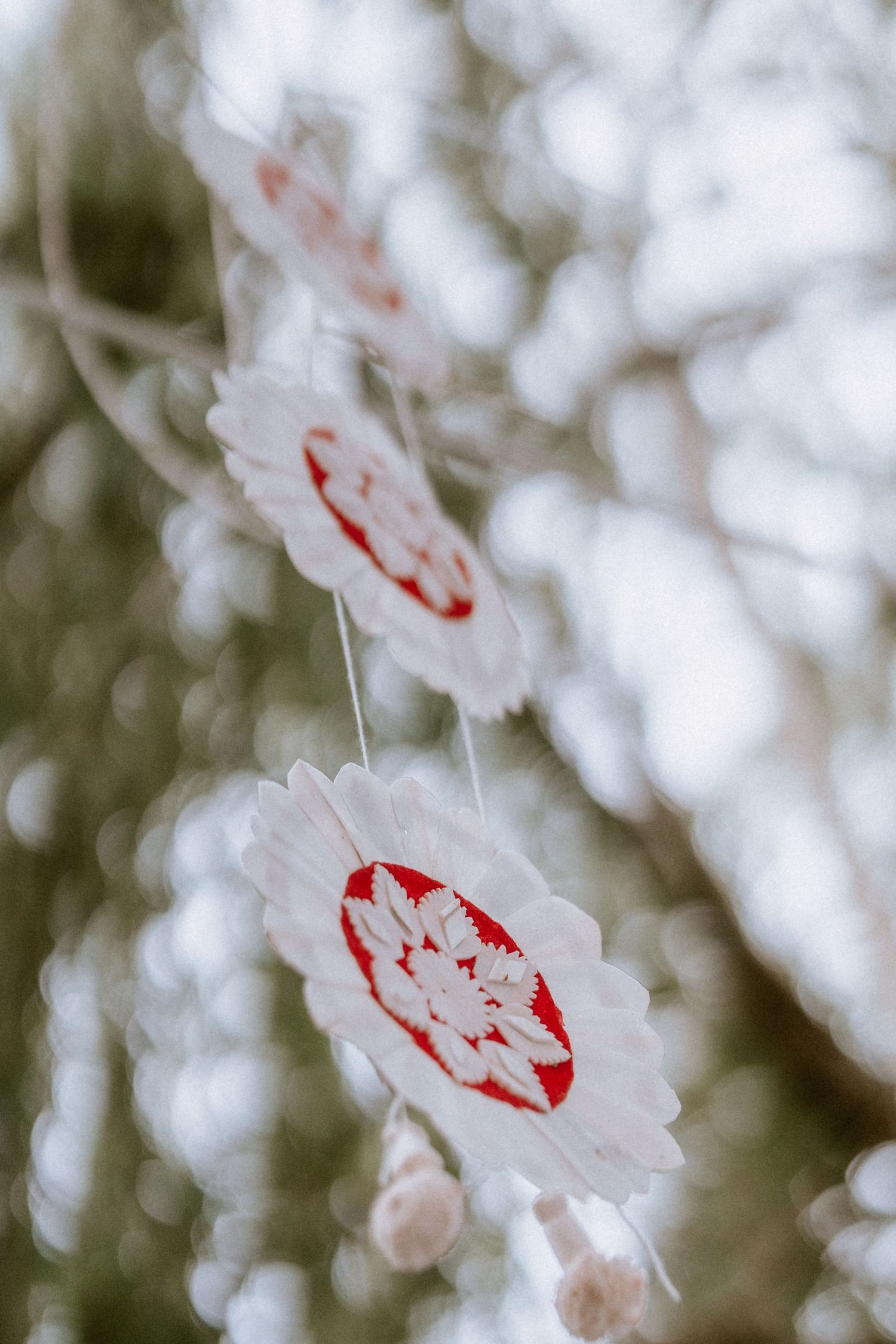 Delicate white paper decorations with red accents hanging against a soft bokeh background.