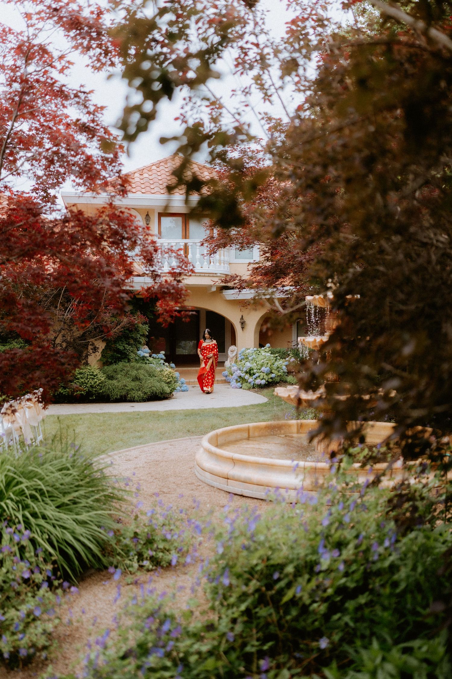A curved garden pathway with red maple trees and purple flowers leading to a building entrance.
