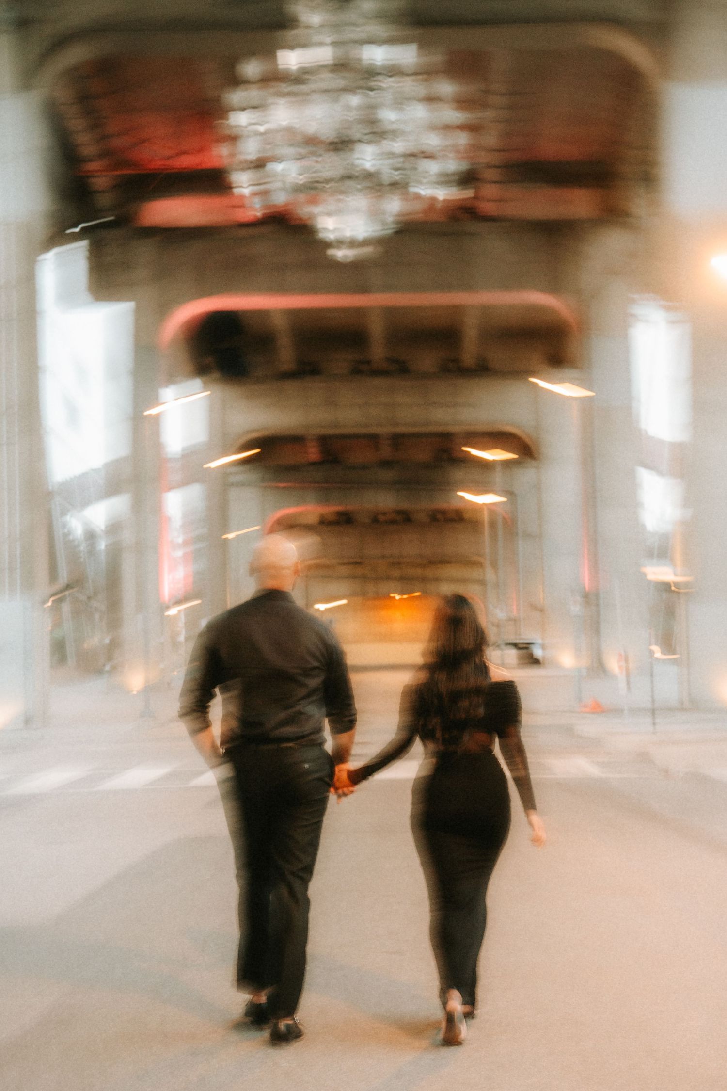 Blurred motion shot of two people walking through an industrial hallway with warm lighting and concrete walls.