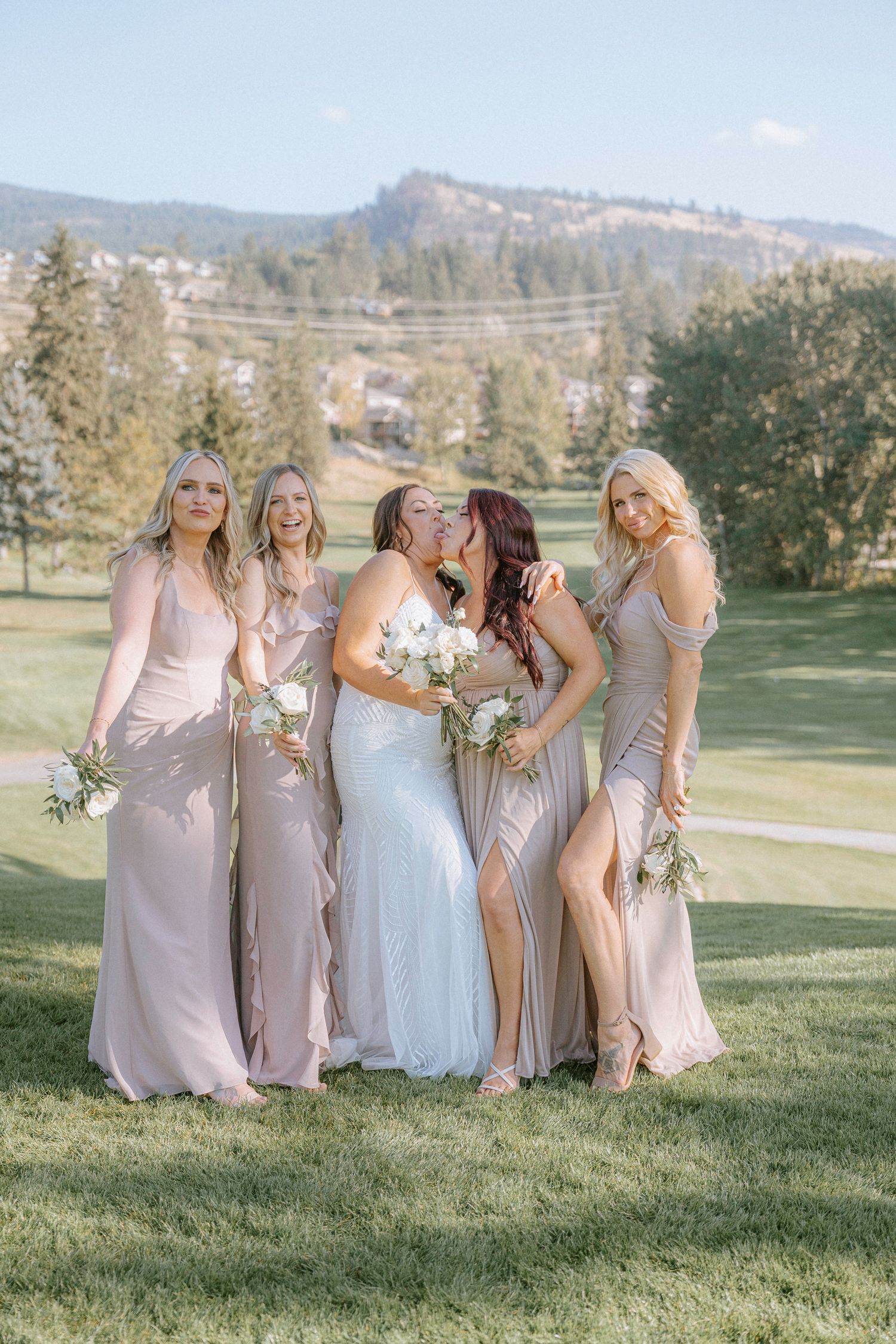 Bridal party in blush pink dresses posing on a hillside golf course.
