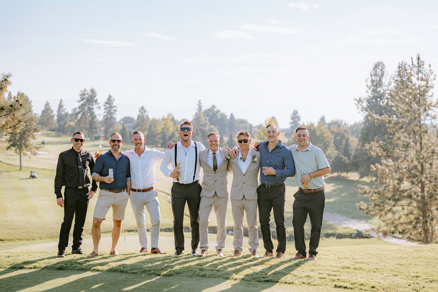 Groomsmen in casual attire posing together on a sunny golf course with mountain views.