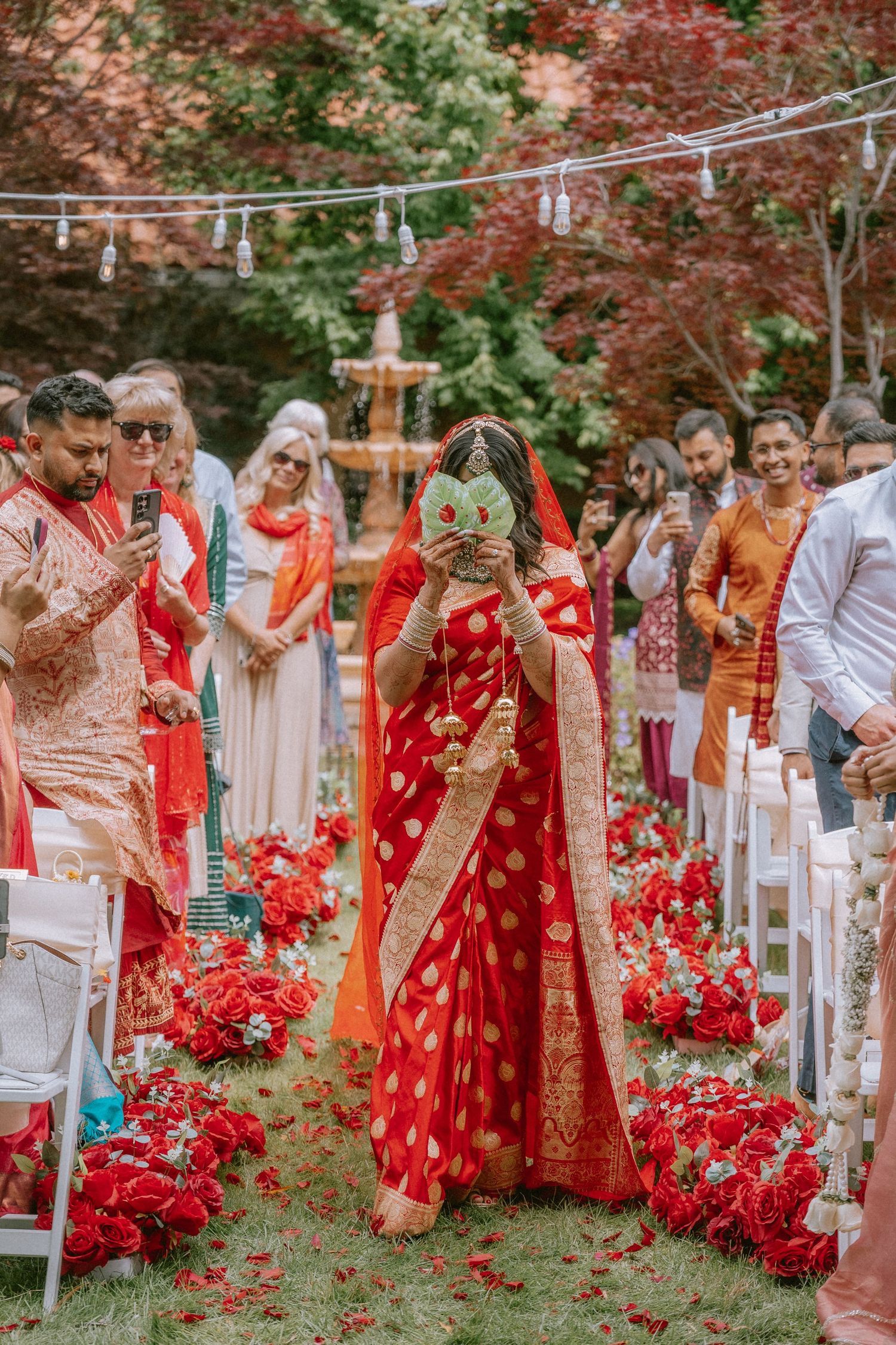 Traditional Indian wedding ceremony with guests in colorful attire and red floral decorations.