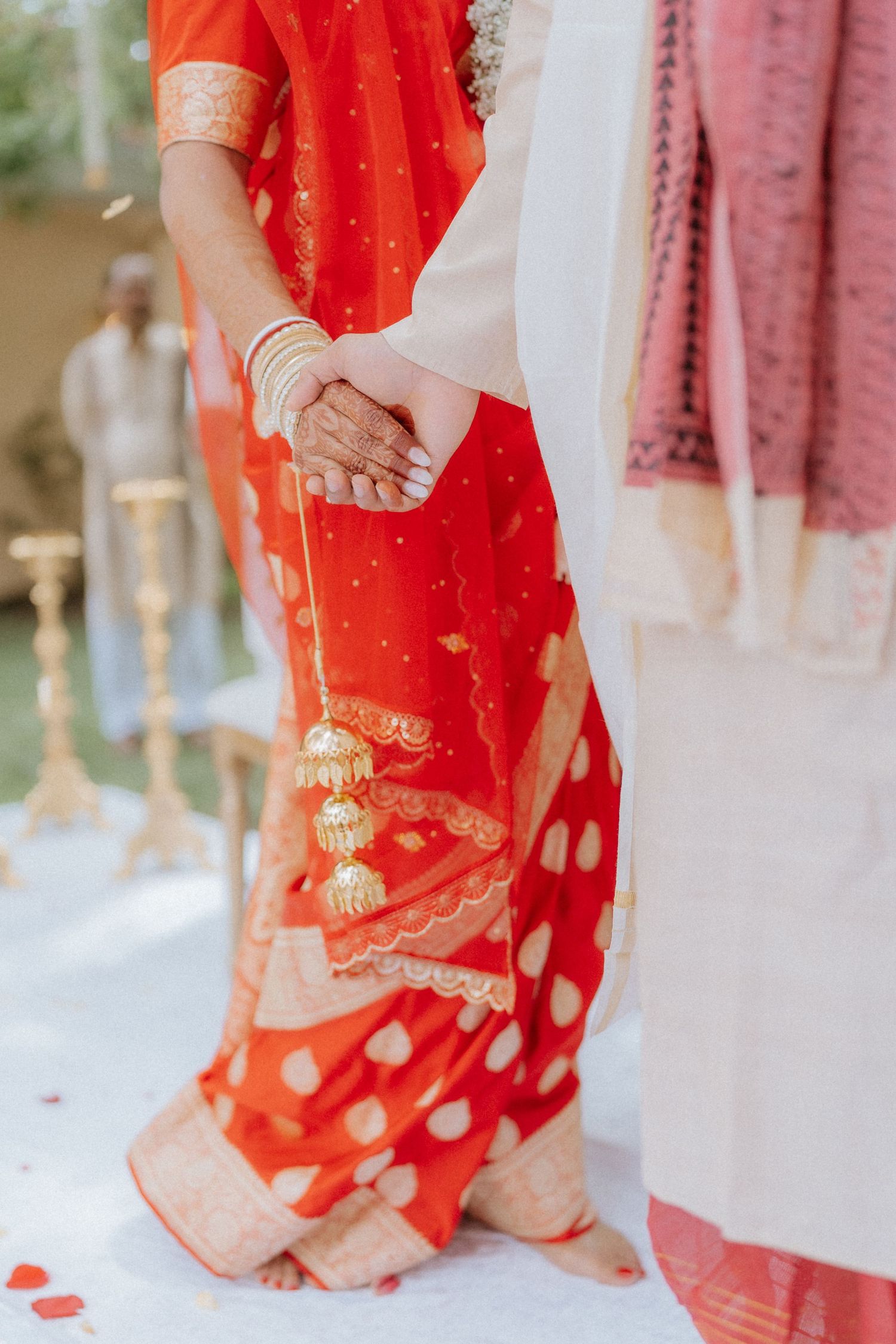 Detail shot of traditional Indian wedding attire showing red and gold sari fabric and joined hands.