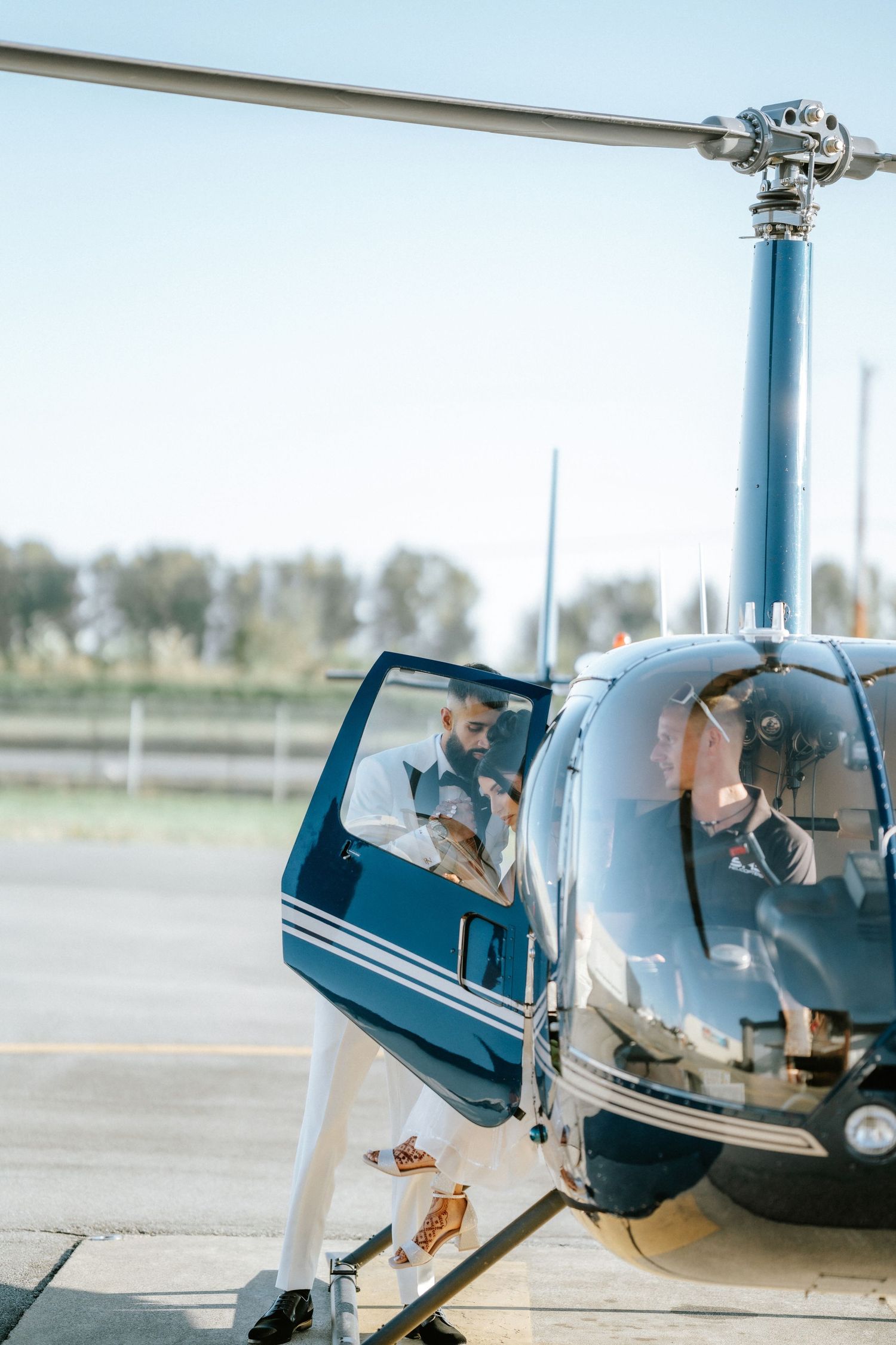 A blue and white helicopter sits on the tarmac with open doors and occupants visible inside.