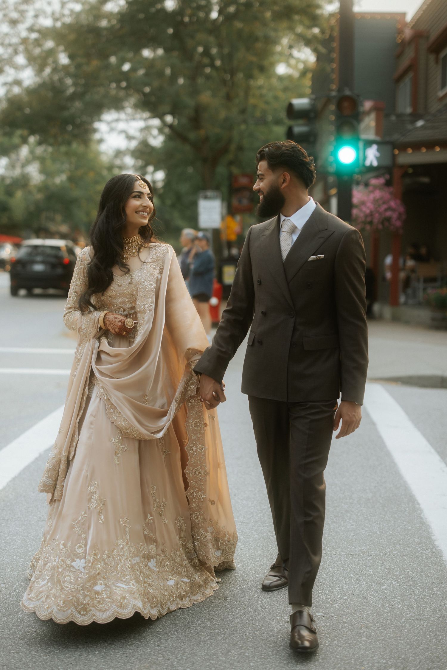 A couple in traditional South Asian wedding attire walking together on a city street at dusk.