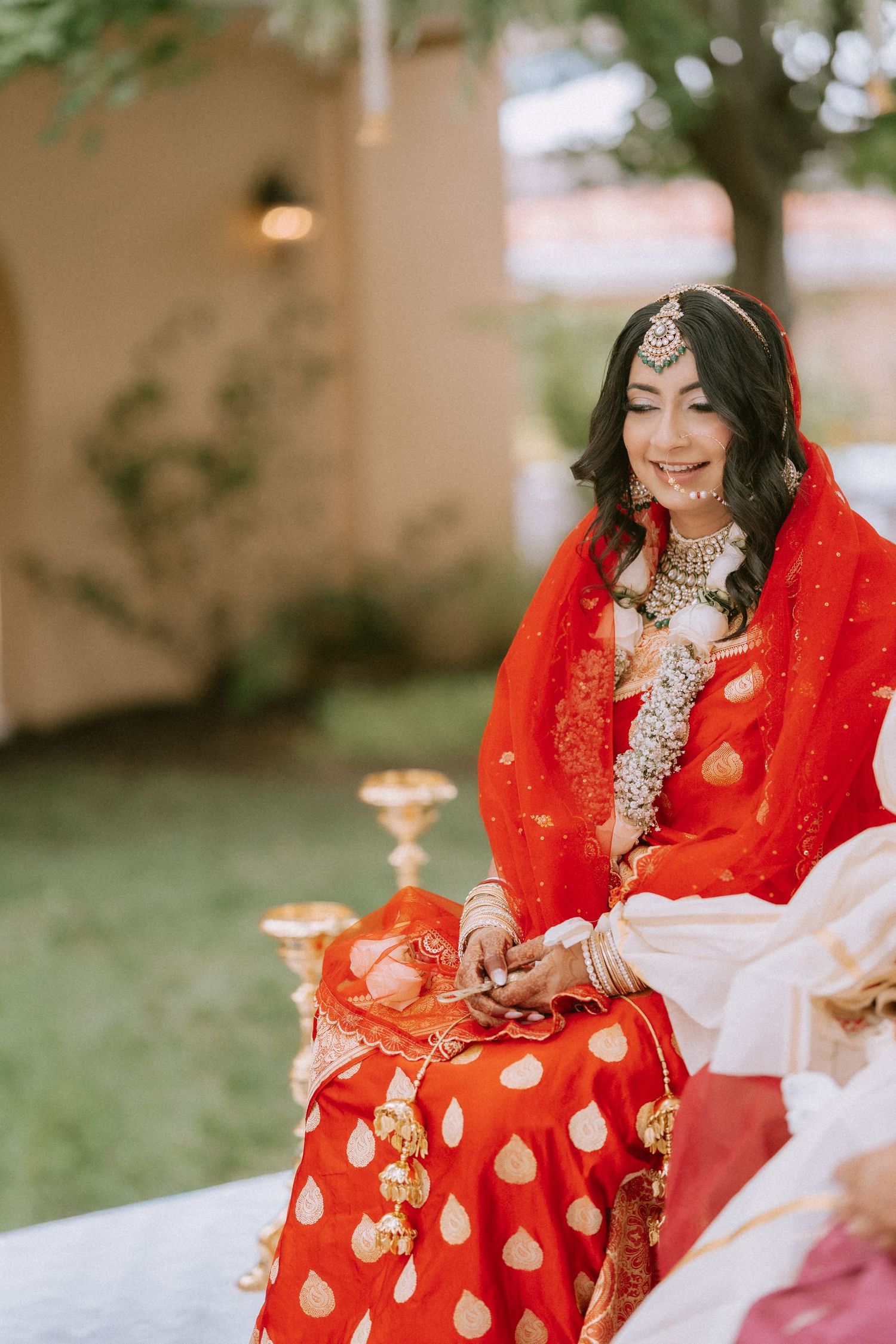 Person wearing a vibrant red and gold traditional South Asian wedding outfit sitting outdoors.