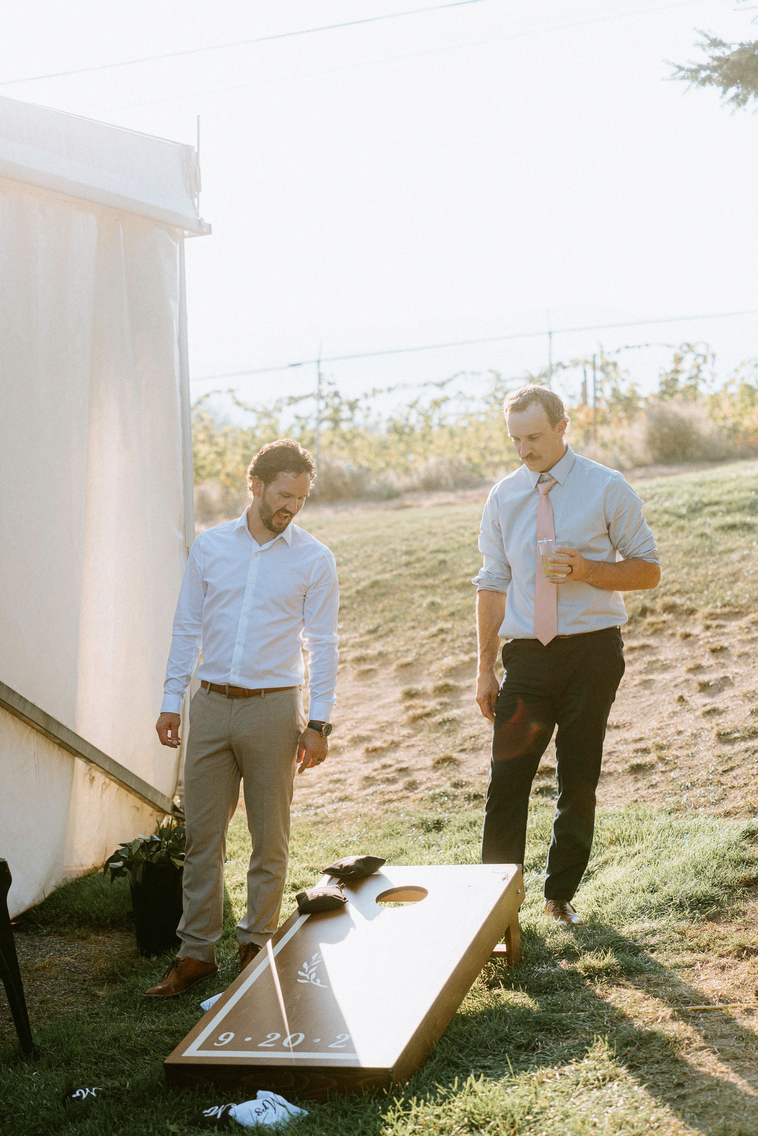 People playing cornhole outdoors at a wedding reception during golden hour.