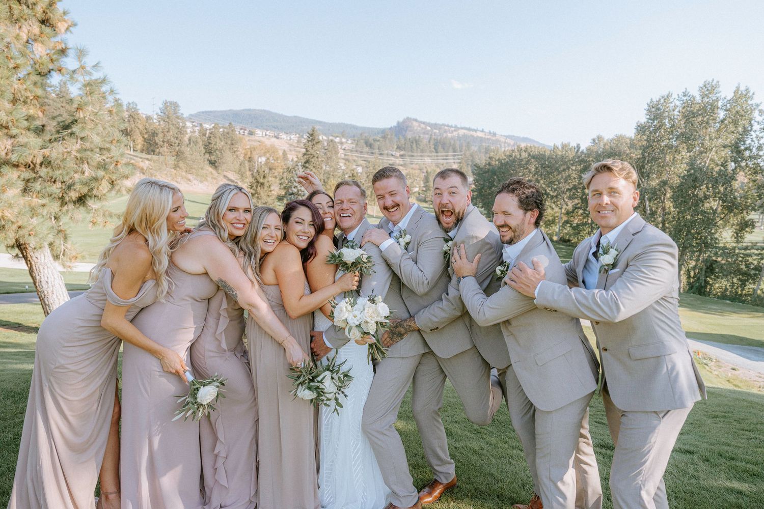 Wedding party in light gray and blush attire poses together on a golf course.