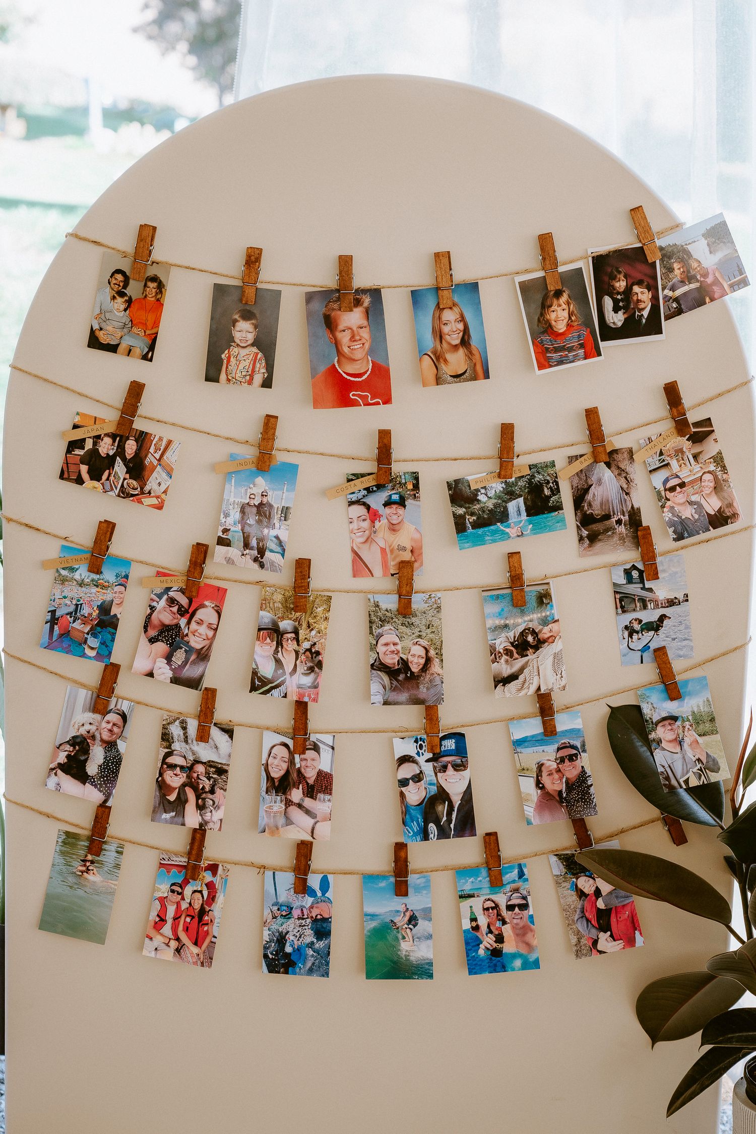Photo display wall with vintage-style snapshots hung on strings with wooden clothespins in an arch formation.