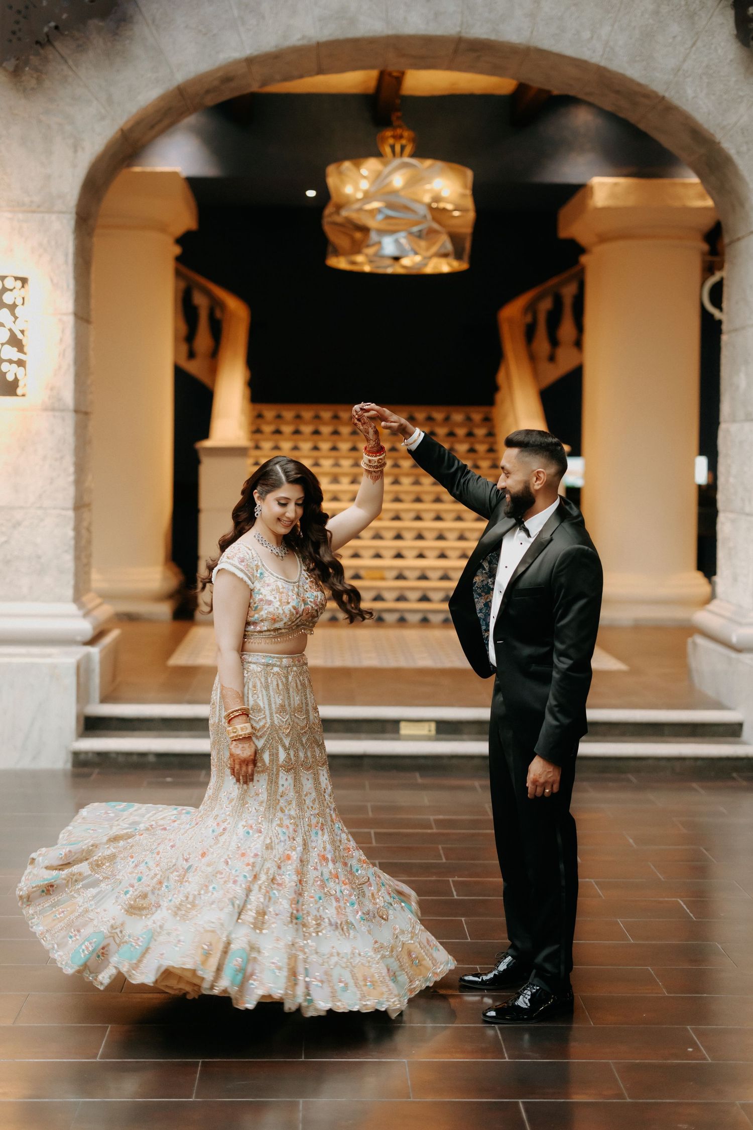 Couple dancing together in an elegant archway setting with the bride wearing a detailed cream and gold gown.