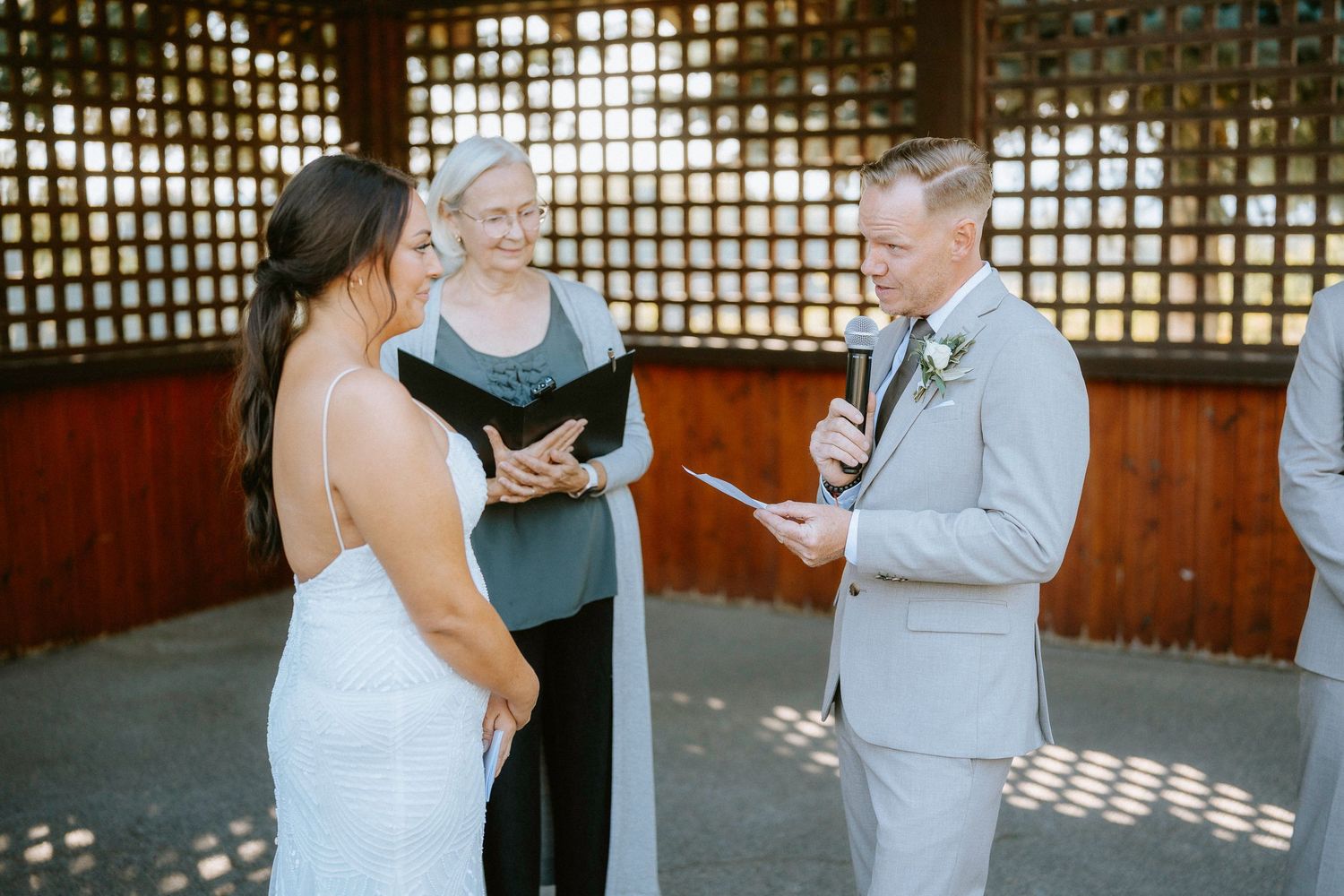 Wedding ceremony taking place in a wooden gazebo with lattice details.