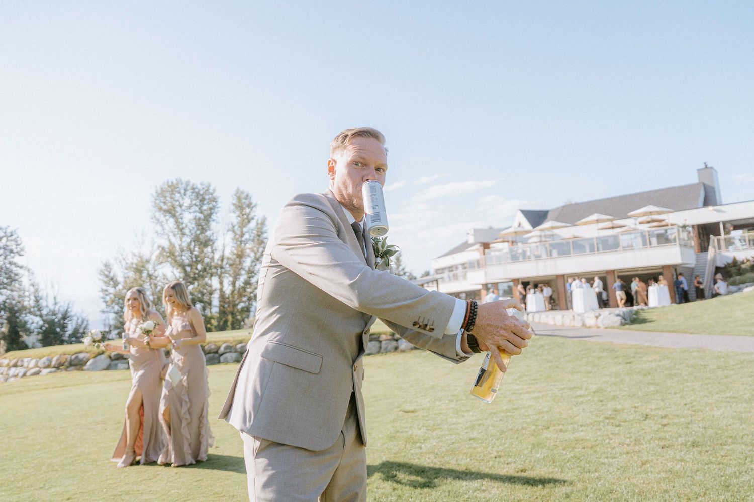 A couple poses on a scenic hillside lawn with guests visible in the background during a wedding celebration.