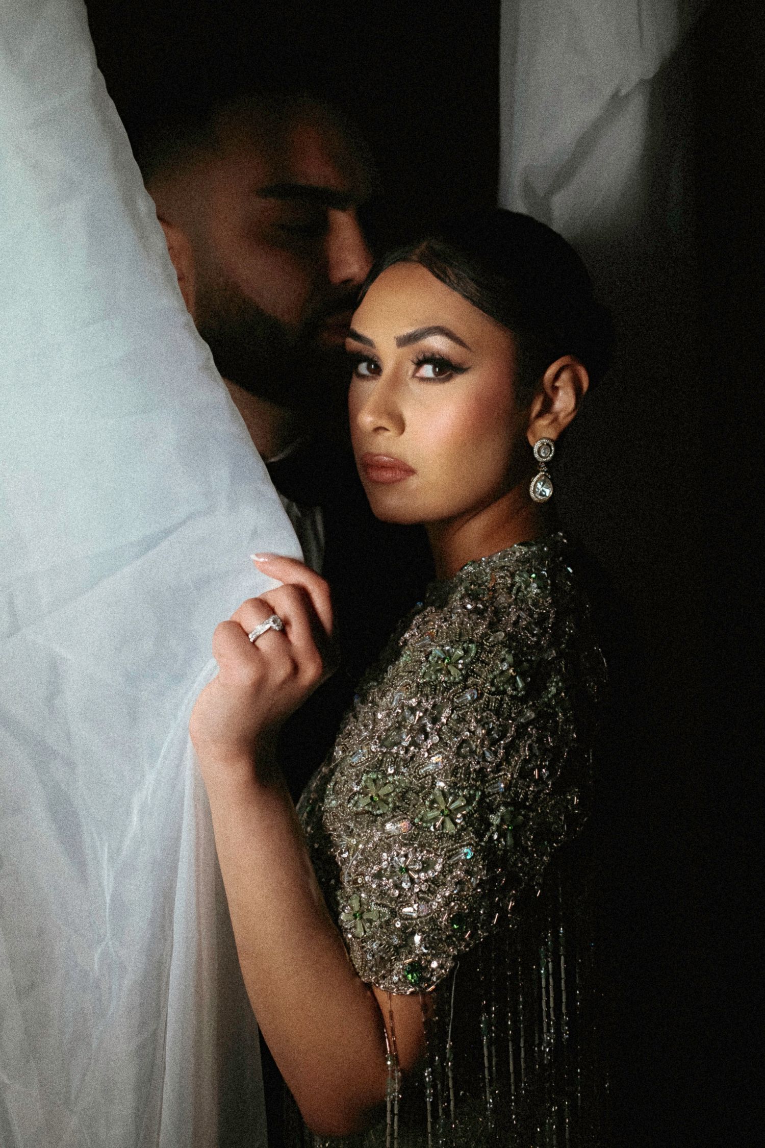 Dramatic portrait series showing a figure in a glittering beaded dress against a dark background with white draping.