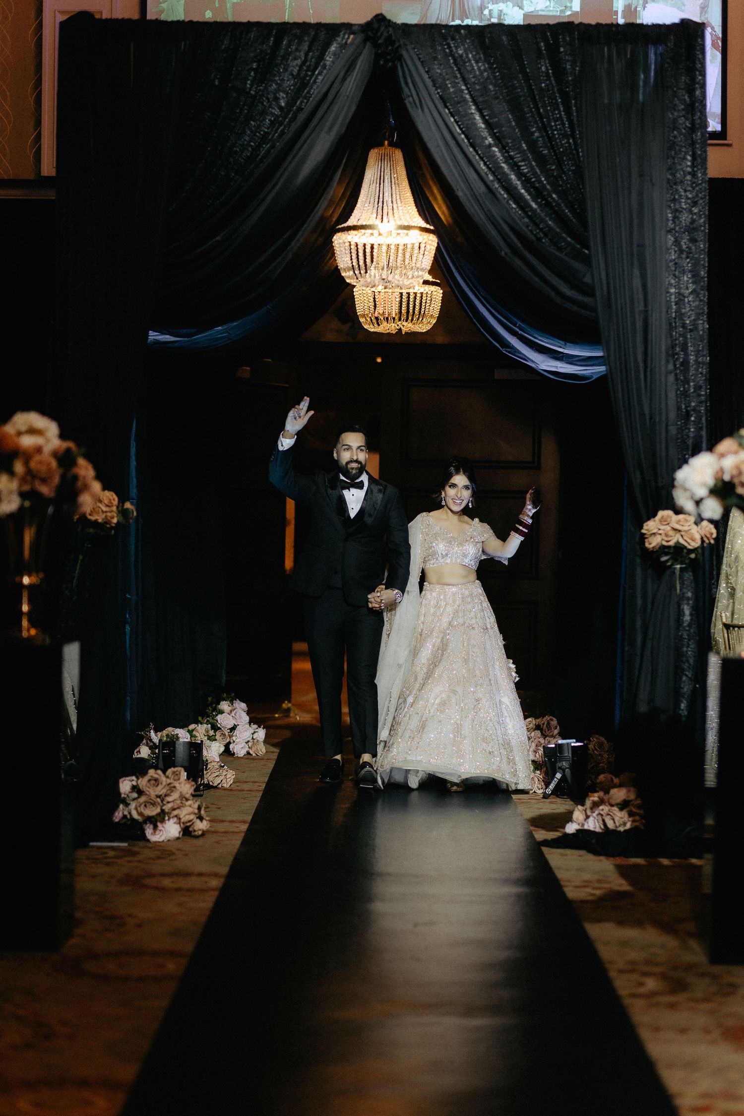 Wedding reception venue with black drapes, chandeliers, and floral arrangements creating a dramatic atmosphere.