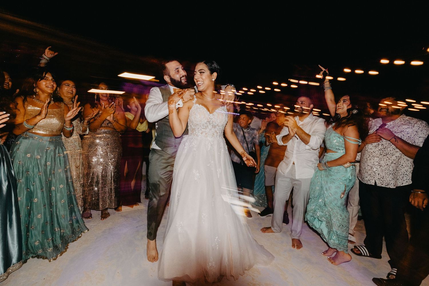 Wedding guests dancing and celebrating together on a dimly lit dance floor at an evening reception.
