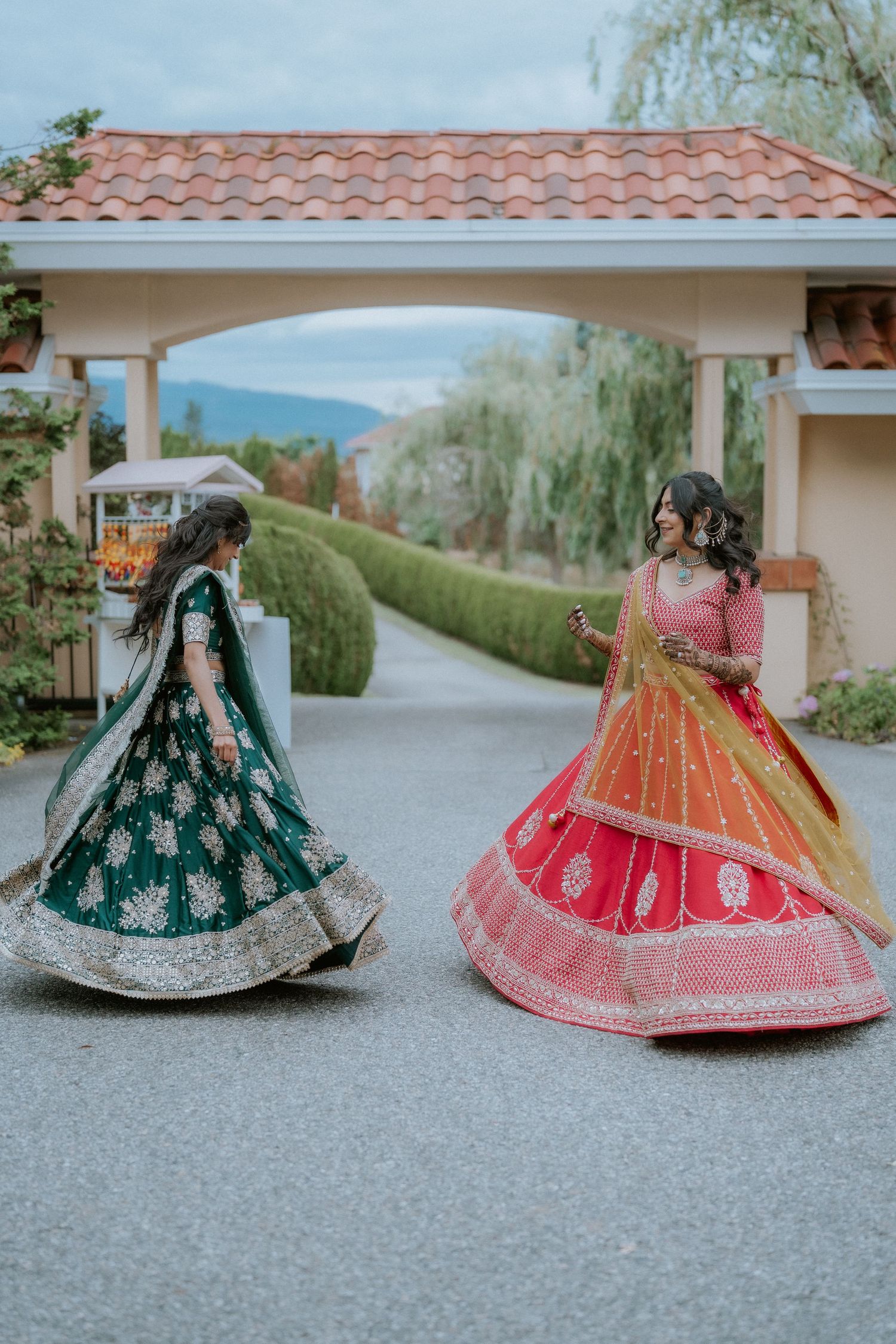 Traditional South Asian wedding lehengas in vibrant green, red and gold colors displayed outdoors on a paved surface.