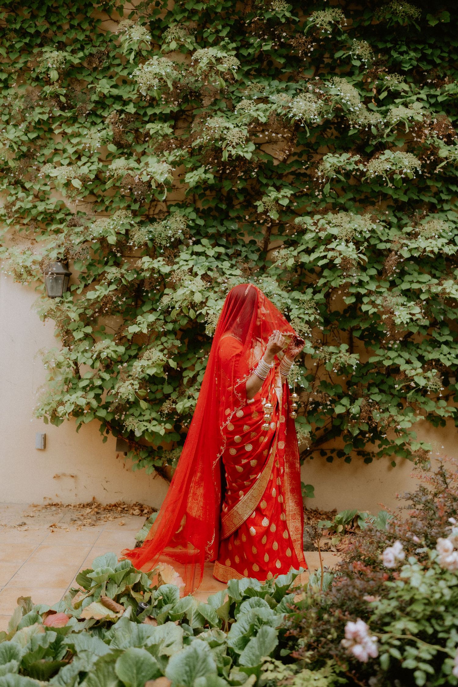 Traditional red Indian bridal attire photographed against a lush green garden backdrop.