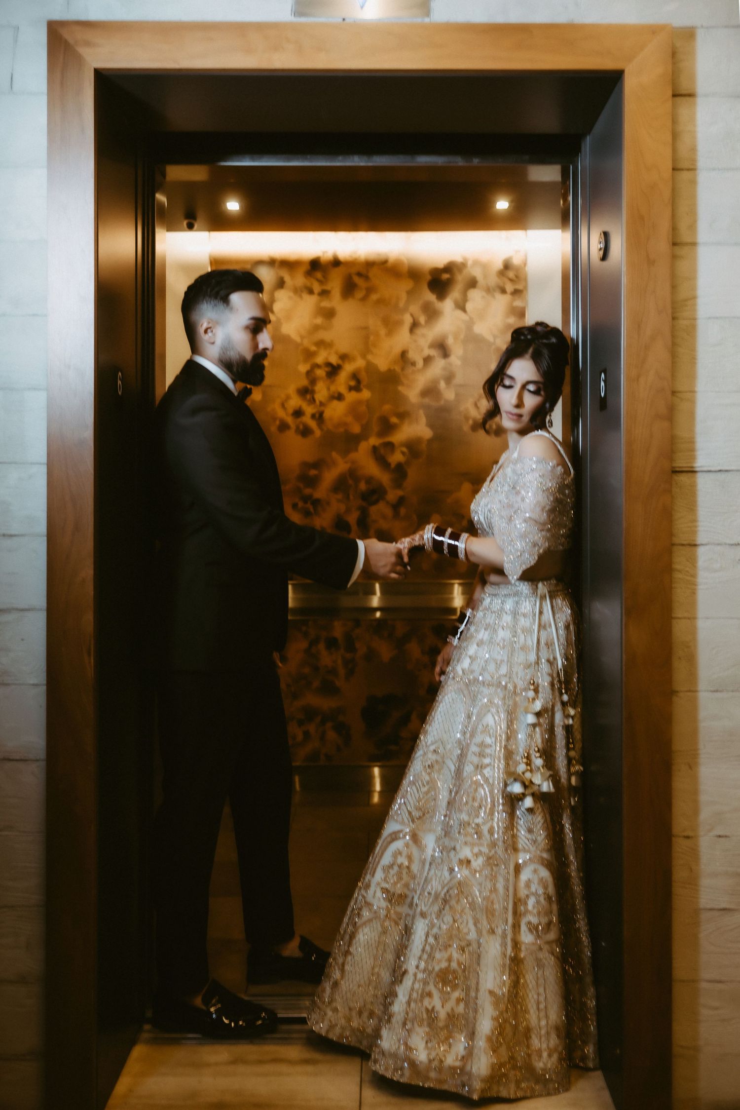 A couple in wedding attire shares intimate moments in a hallway with elegant gold patterned wallpaper.