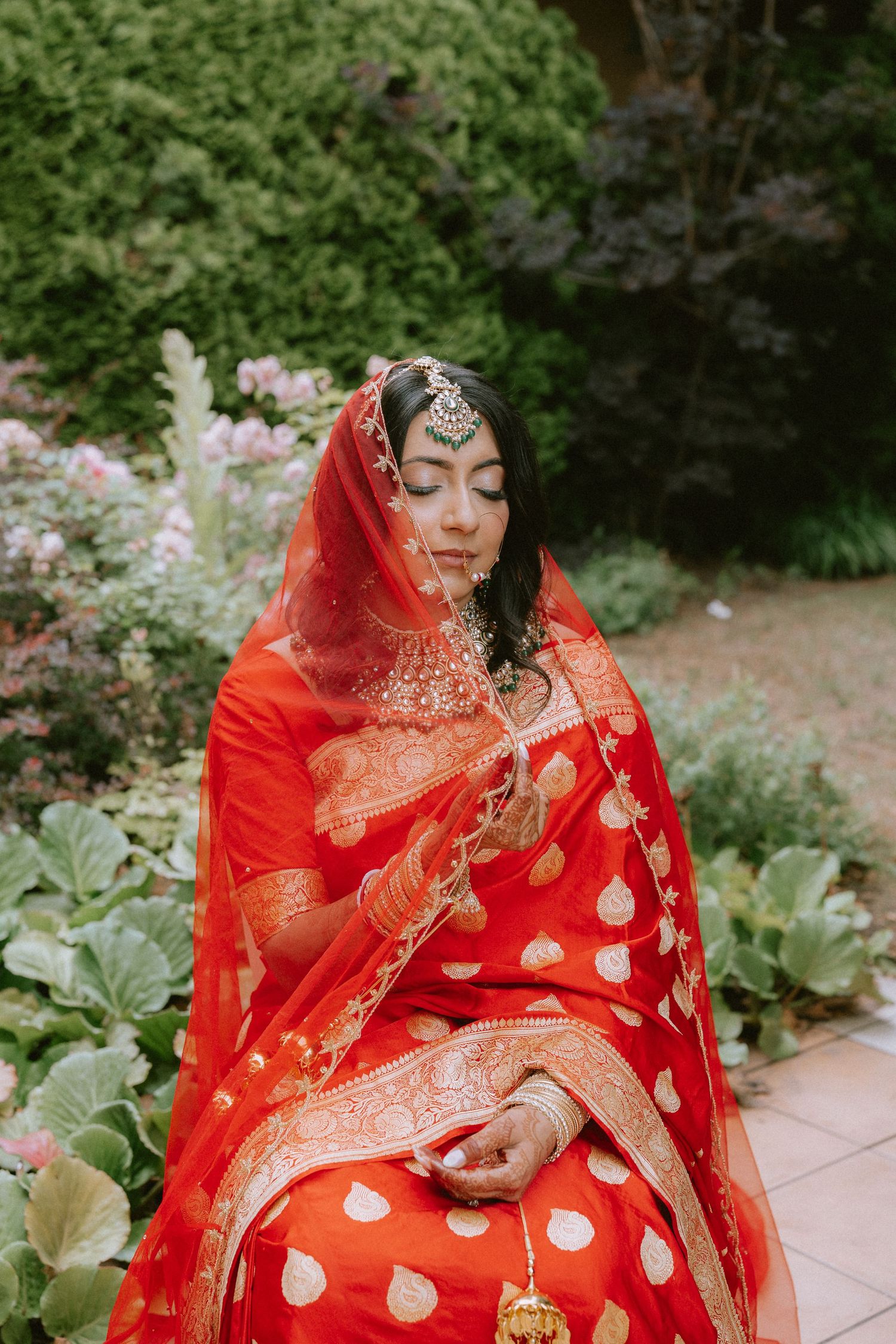 Traditional Indian bridal attire featuring a vibrant red and gold sari in a garden setting.