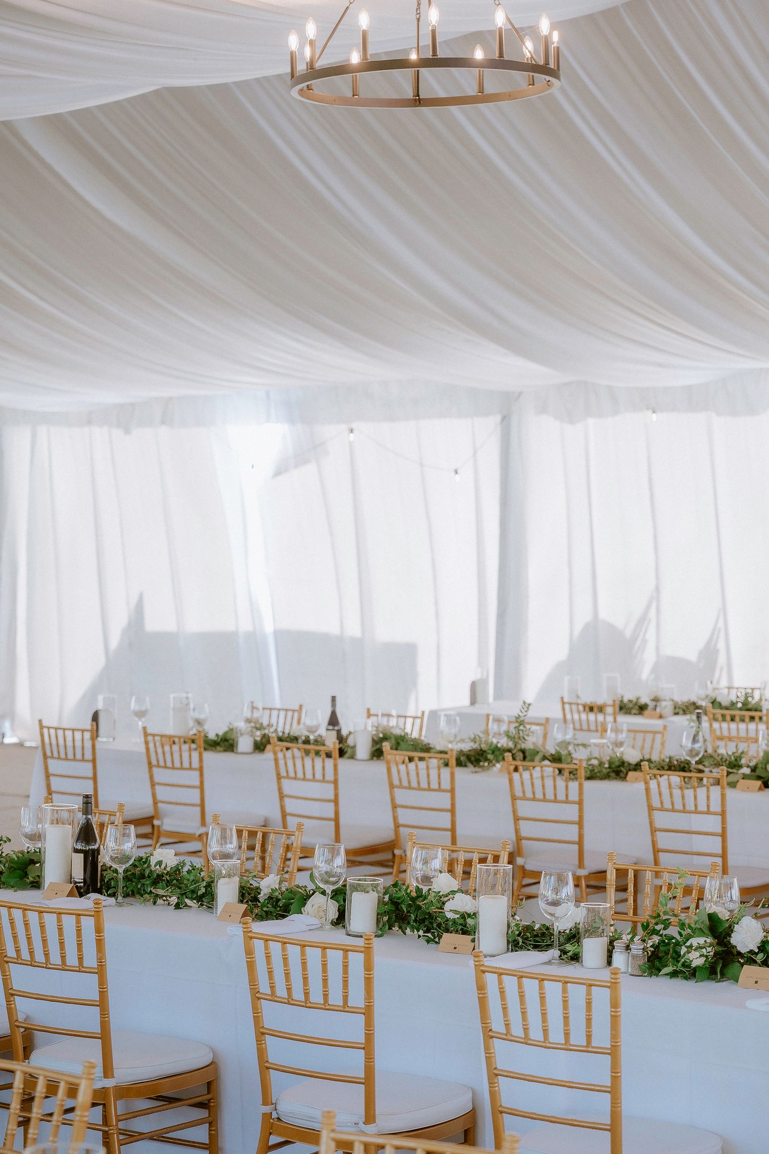 White draped tent interior with wooden chiavari chairs set up for a wedding ceremony.