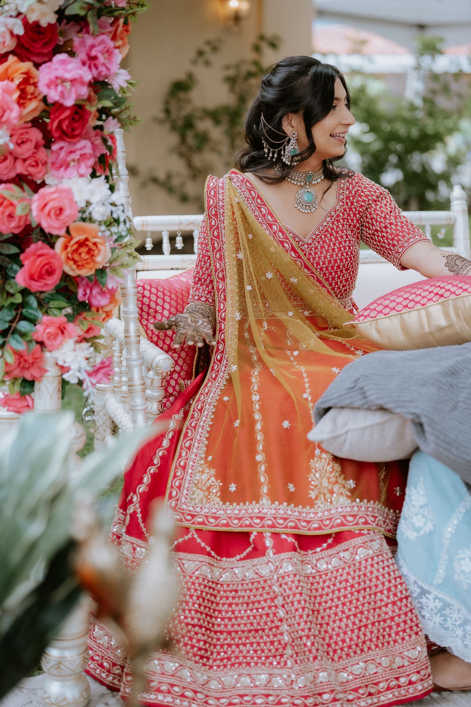 Detailed view of an ornate pink and gold lehenga with pearl embellishments and floral decorations at an outdoor event.