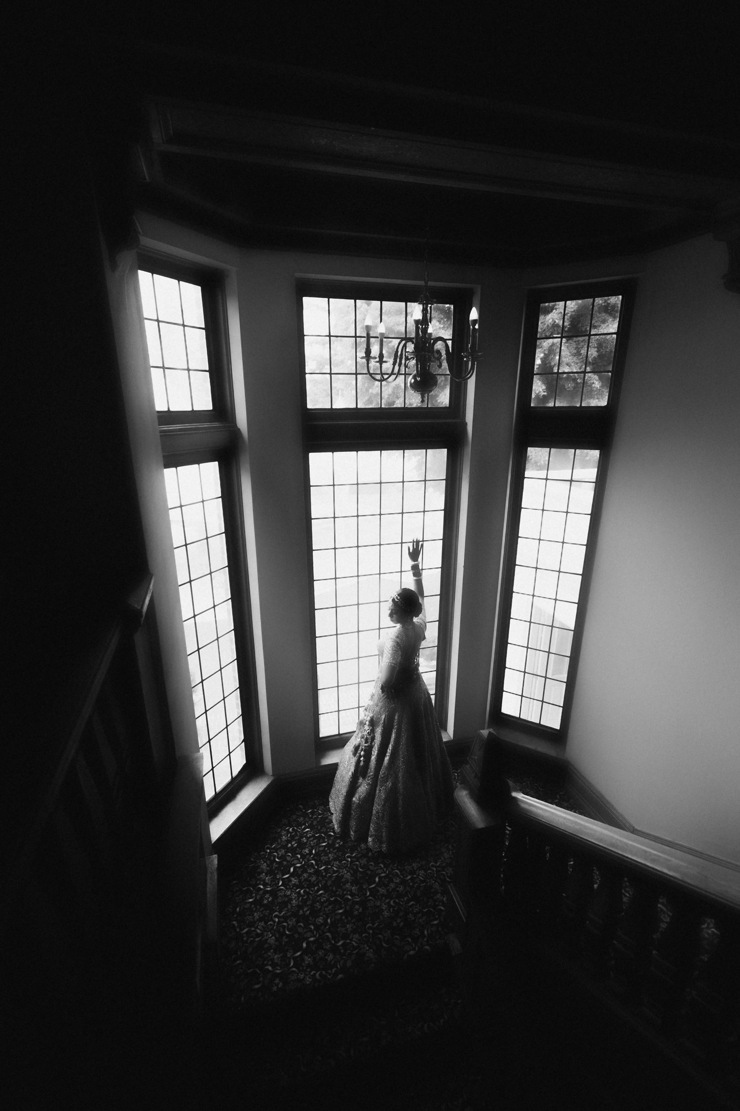 A silhouetted figure in a dress stands by a large bay window with paned glass in a dramatic black and white composition.