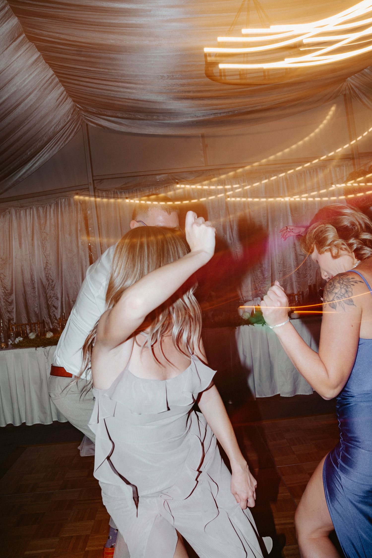 Wedding guests dancing and celebrating on a dance floor under string lights.