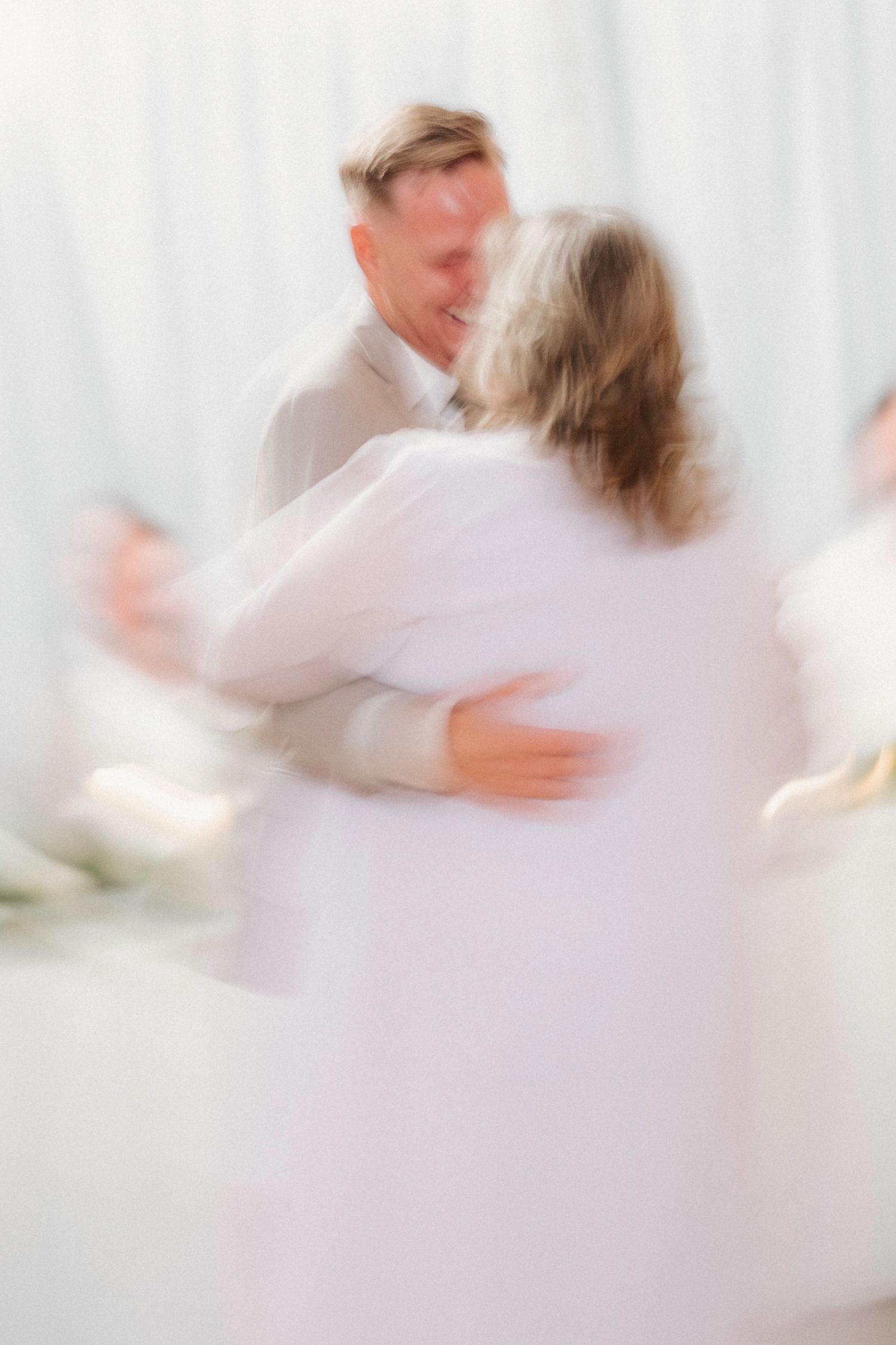 Blurred motion capture of couples dancing in white attire at a wedding reception.