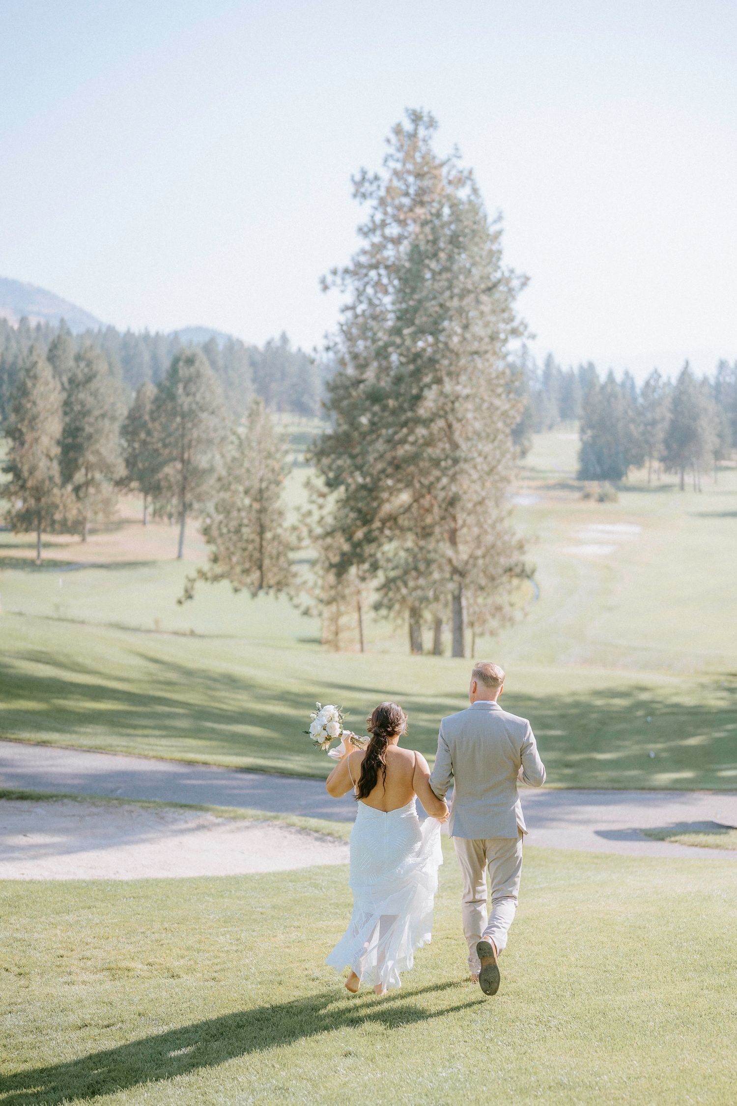 Couple walking hand in hand on a scenic golf course with mountain views.