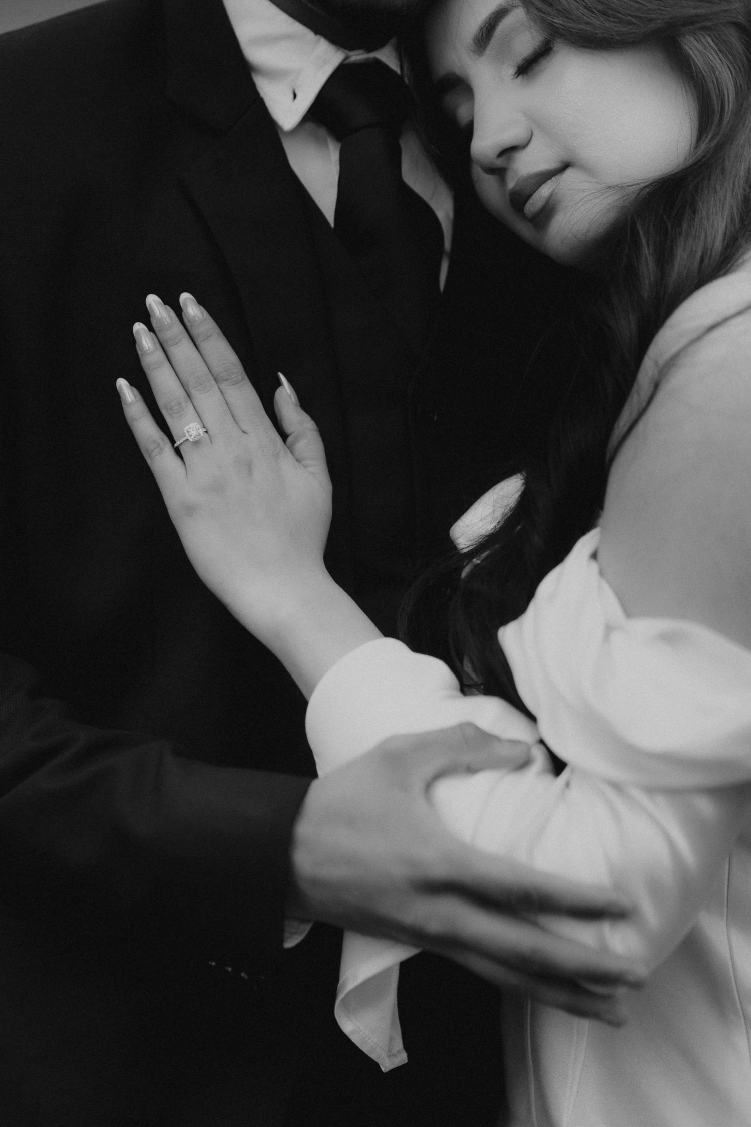 A romantic black and white portrait shows a couple embracing, with the woman's hand displaying an engagement ring.
