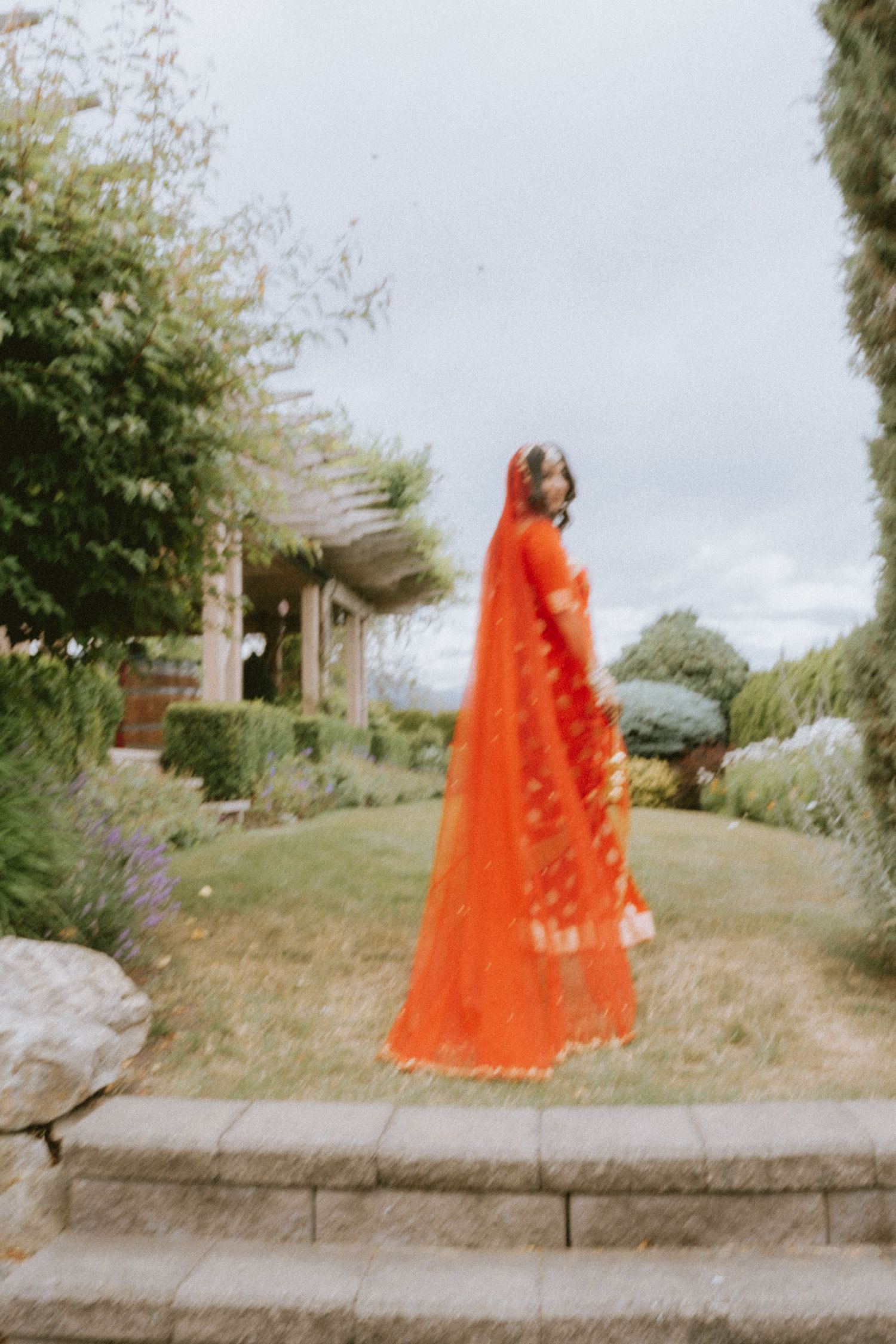 Figure in bright orange traditional wedding attire standing in a garden landscape.