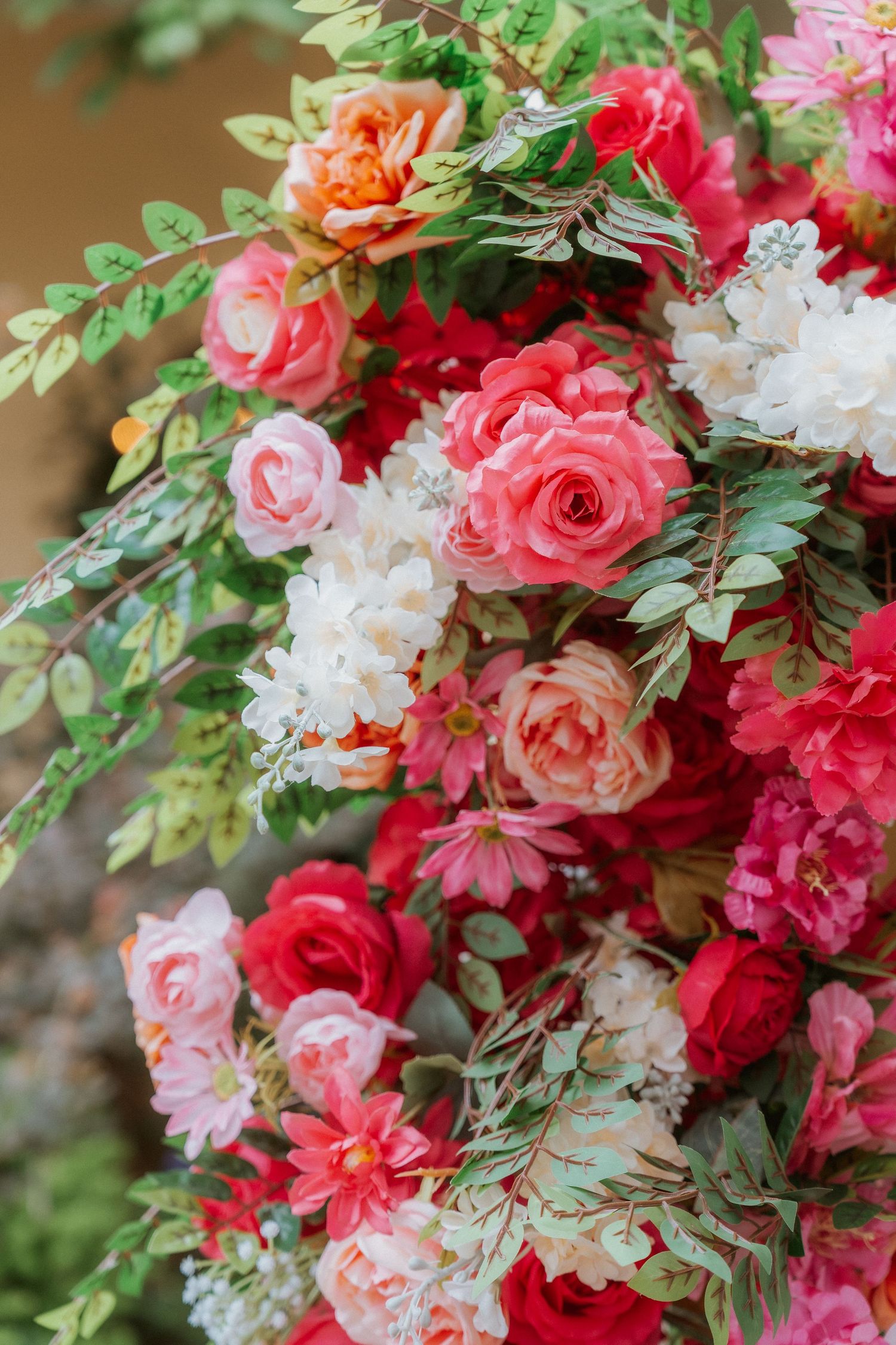 Vibrant floral arch decoration featuring pink roses, red flowers, and white blooms with green foliage for a wedding ceremony.