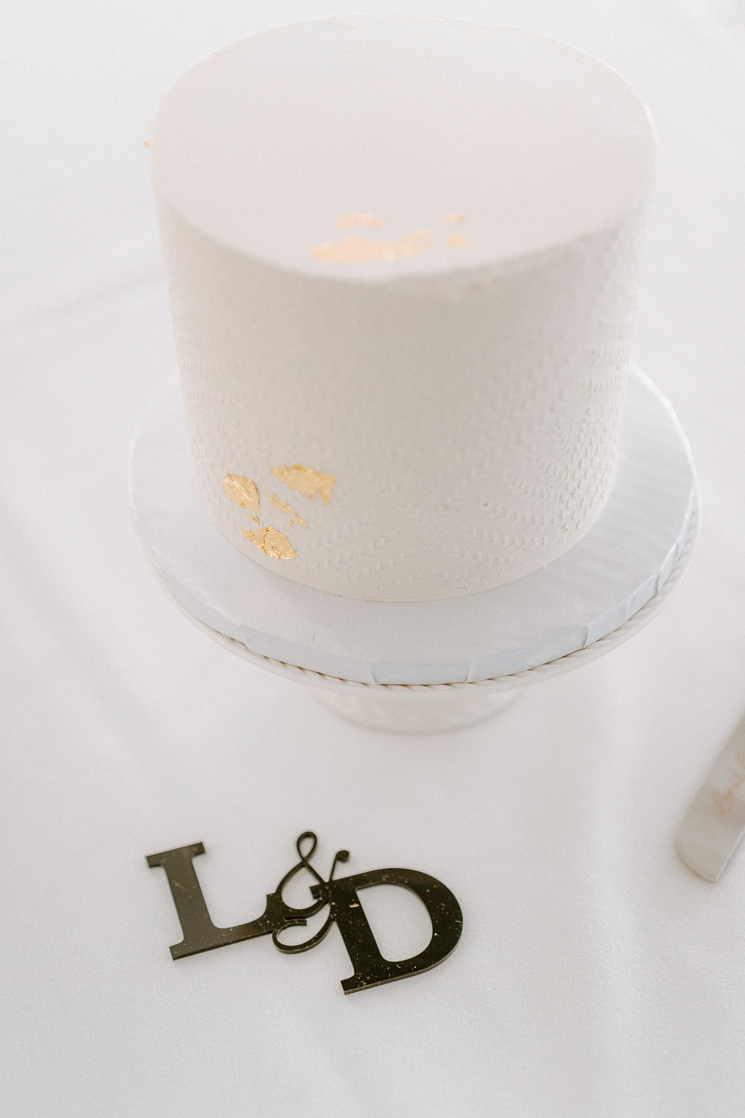Minimalist white wedding cake with metallic lettering decoration.