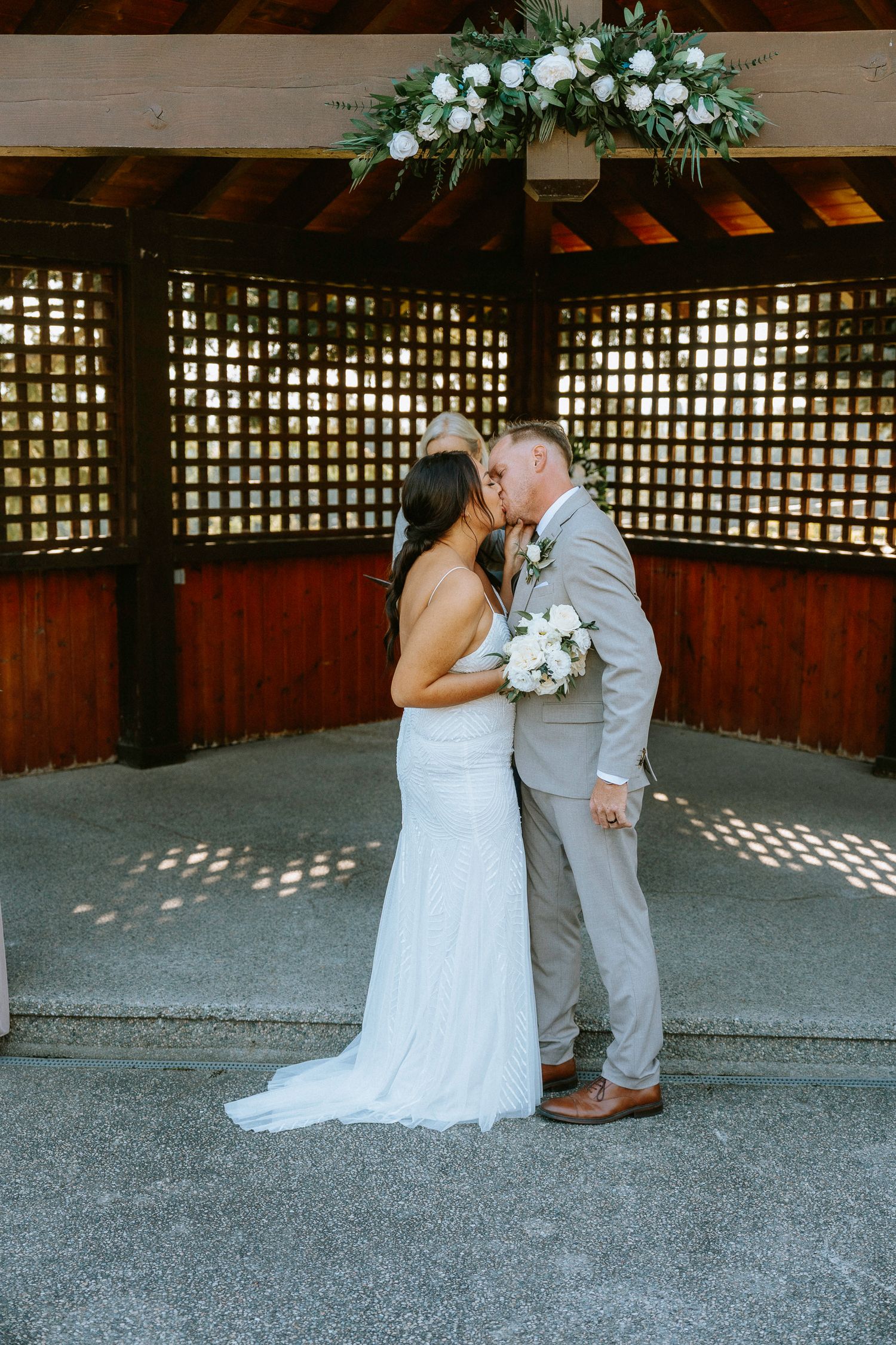 Wedding couple shares intimate moments under a wooden lattice pergola during their ceremony.