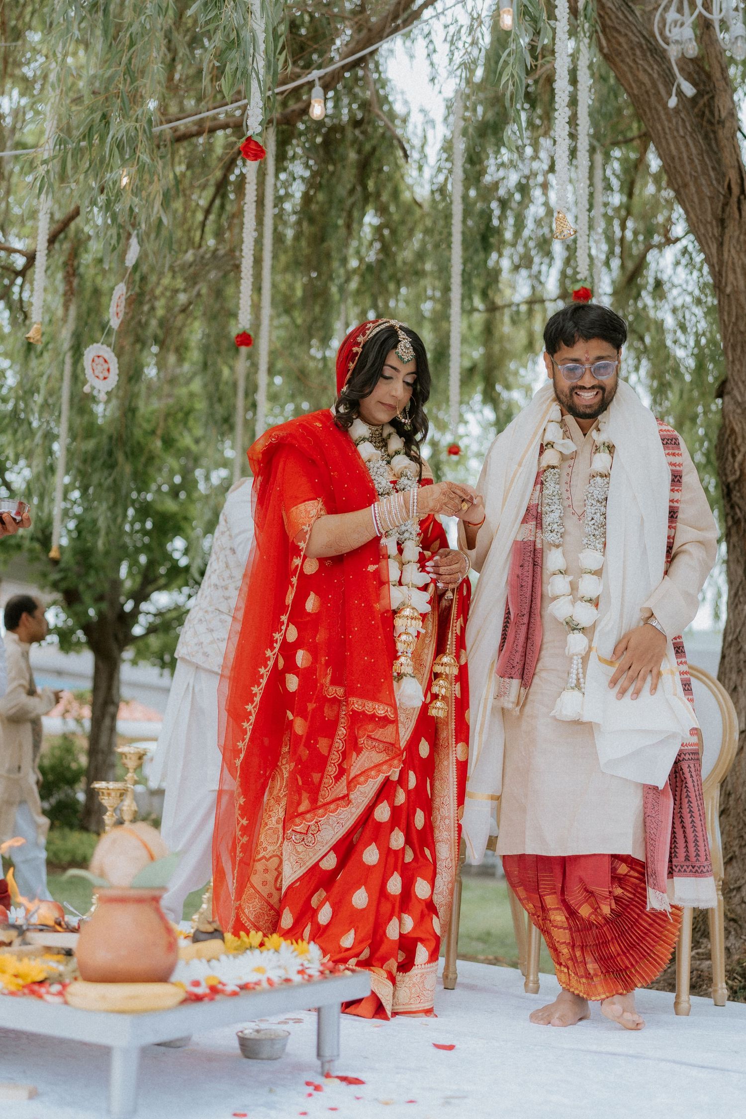 Wedding ceremony participants performing traditional rituals under willow trees.