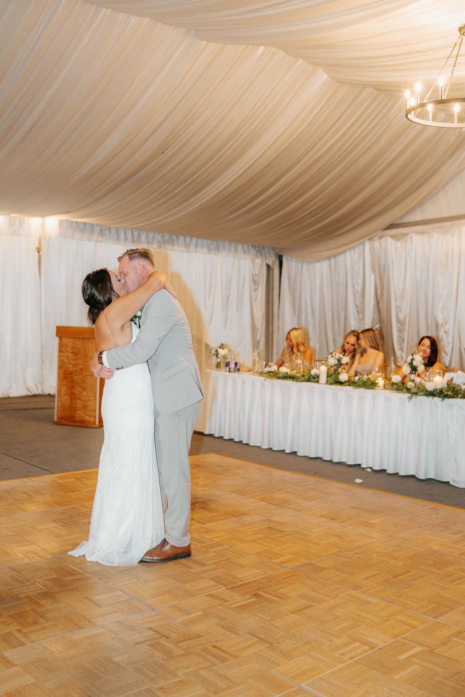 Couple shares their first dance in an elegant white-draped wedding reception tent.