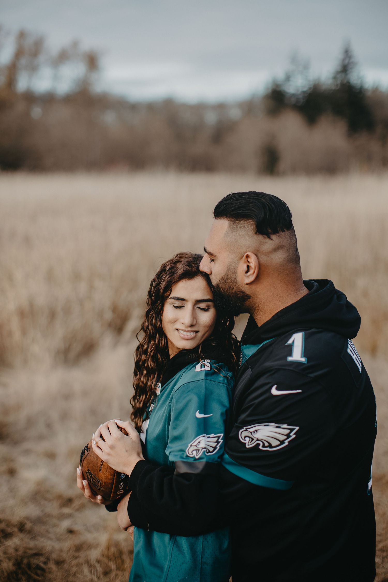 Couple wearing Eagles jerseys embrace in a rustic field during autumn.