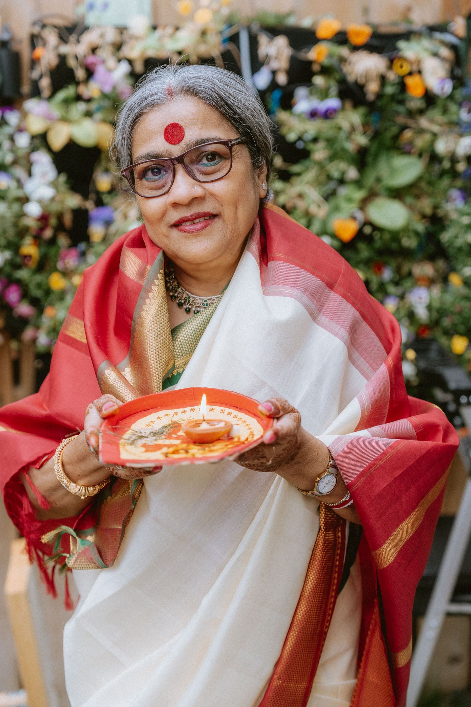 A person wearing traditional white and red attire enjoying pizza with colorful flowers in the background.
