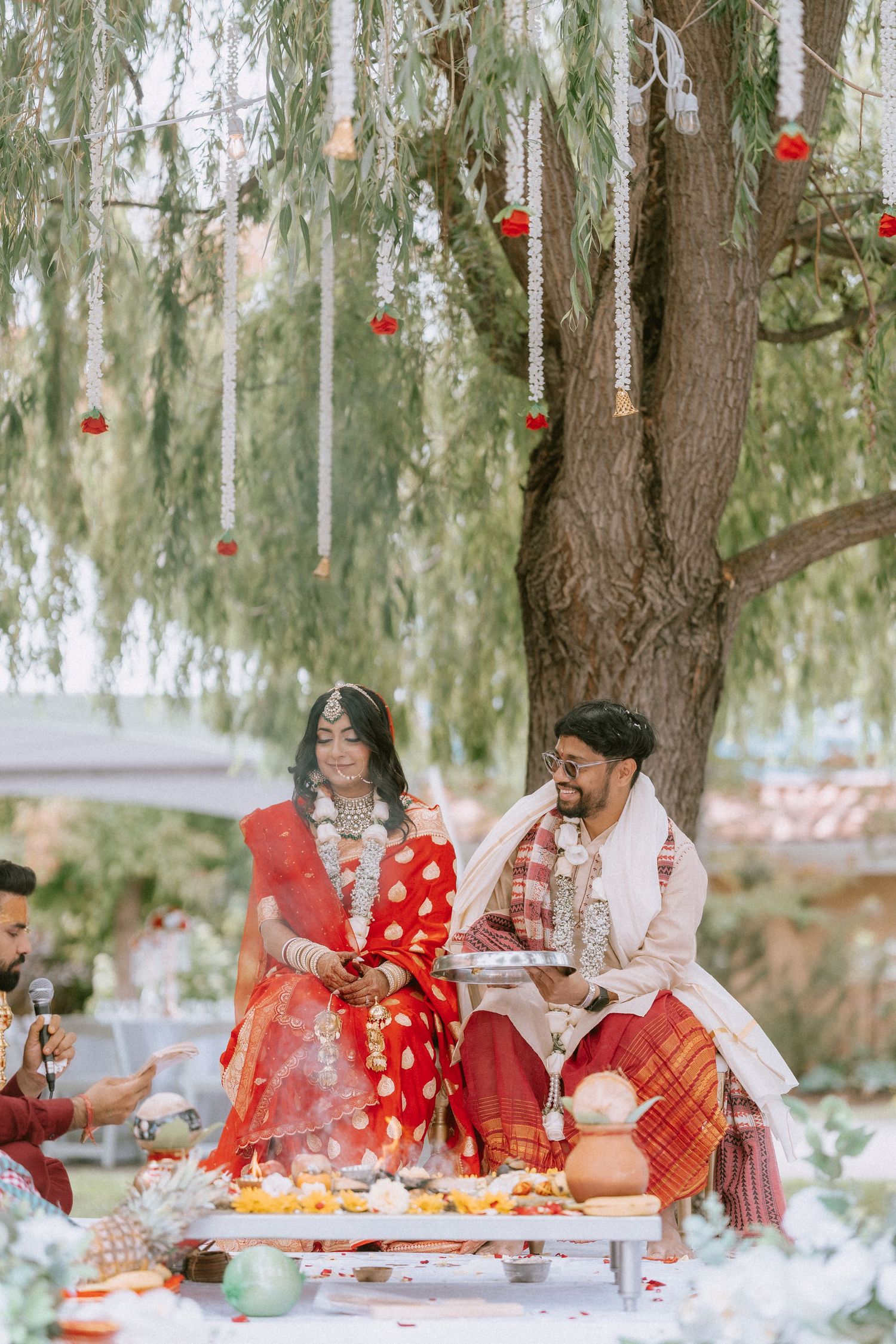 Outdoor tea ceremony under willow trees with traditional red decor and table settings.