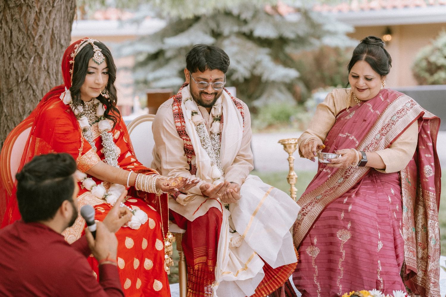 Traditional wedding ceremony with guests in colorful saris and formal attire gathered outdoors.